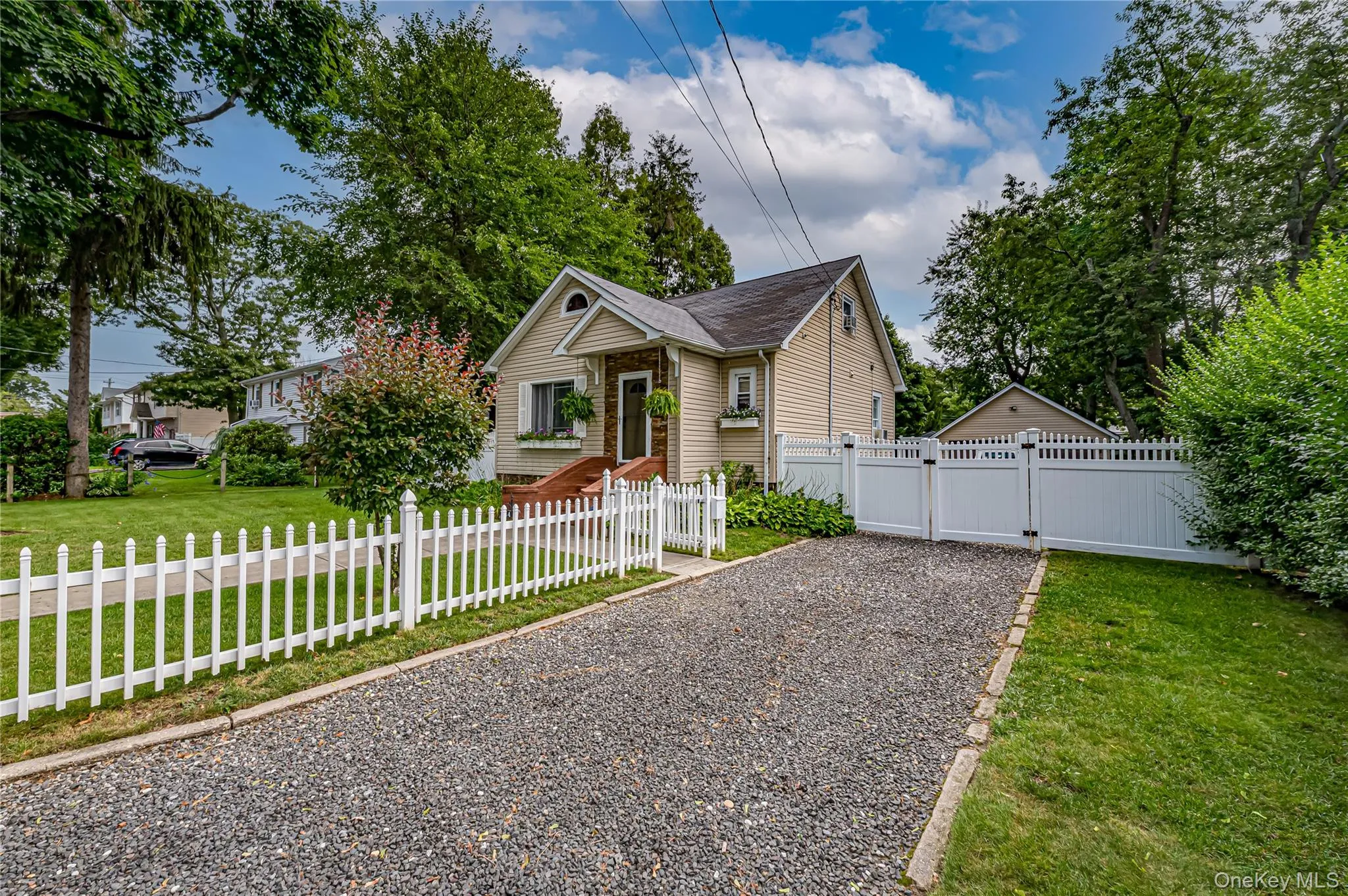 Gravel driveway with a white picket fence and privacy fencing, leading to a light-colored siding home with a peaked roof. Gravel driveway with a white picket fence and privacy fencing, leading to a light-colored siding home with a peaked roof.