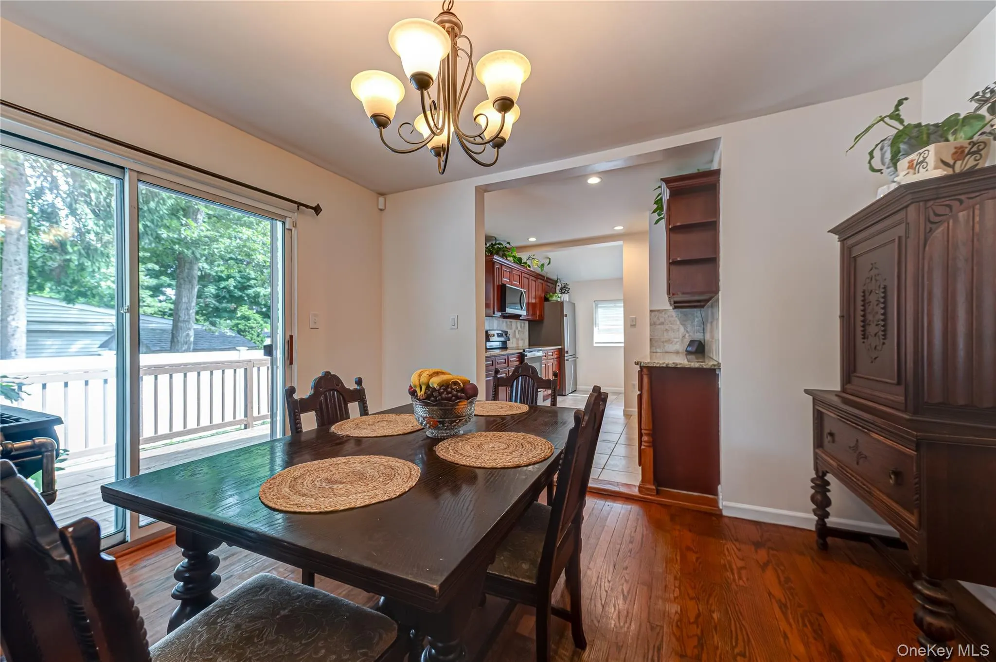 Open-concept dining area featuring wood-finish flooring, a contemporary chandelier, and direct access to an exterior deck via sliding glass doors Open-concept dining area featuring wood-finish flooring, a contemporary chandelier, and direct access to an exterior deck via sliding glass doors