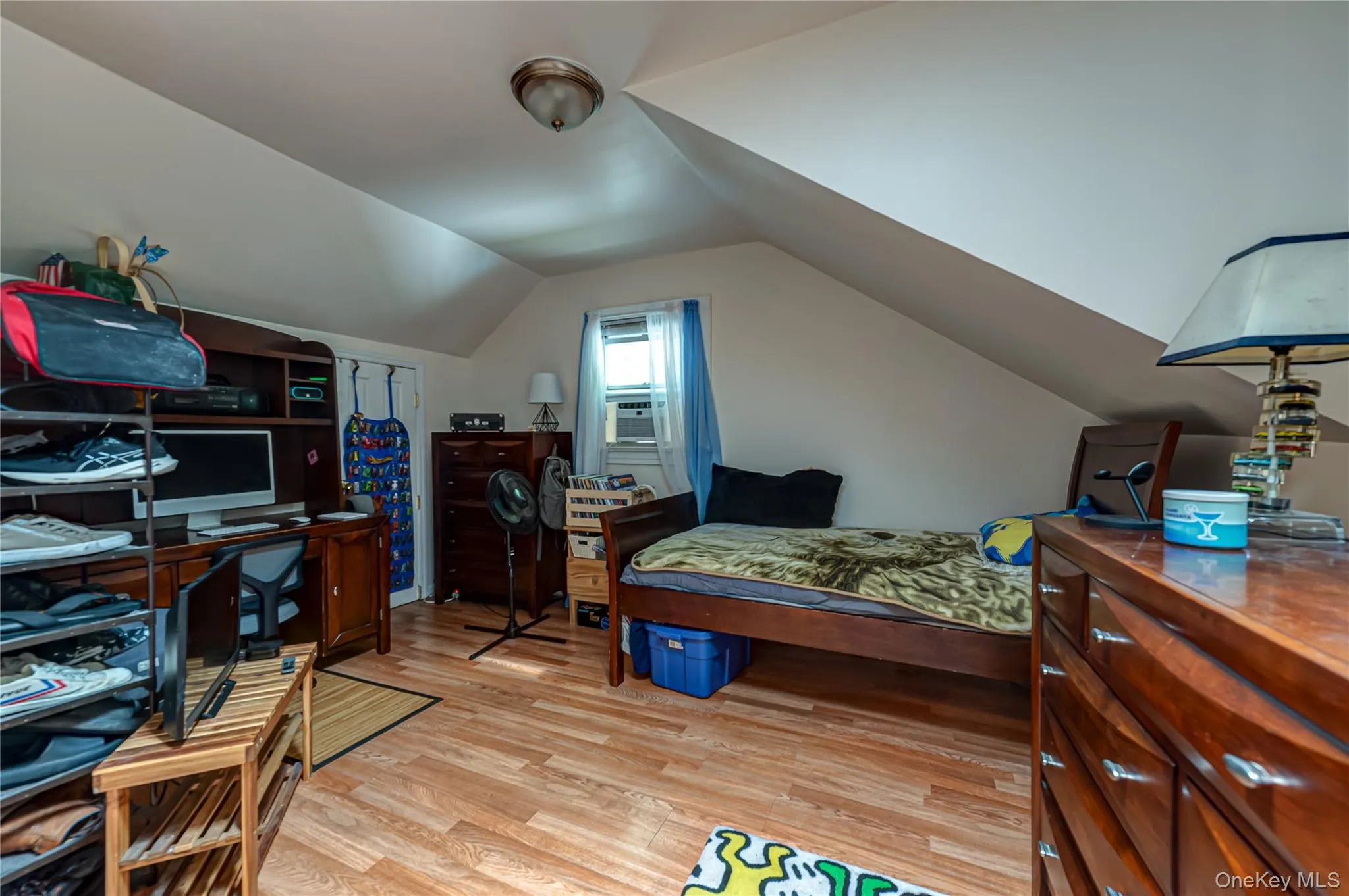 Room featuring wood colored finish flooring, sloped ceilings, and a window with a wall-mounted air conditioning unit Room featuring wood colored finish flooring, sloped ceilings, and a window with a wall-mounted air conditioning unit