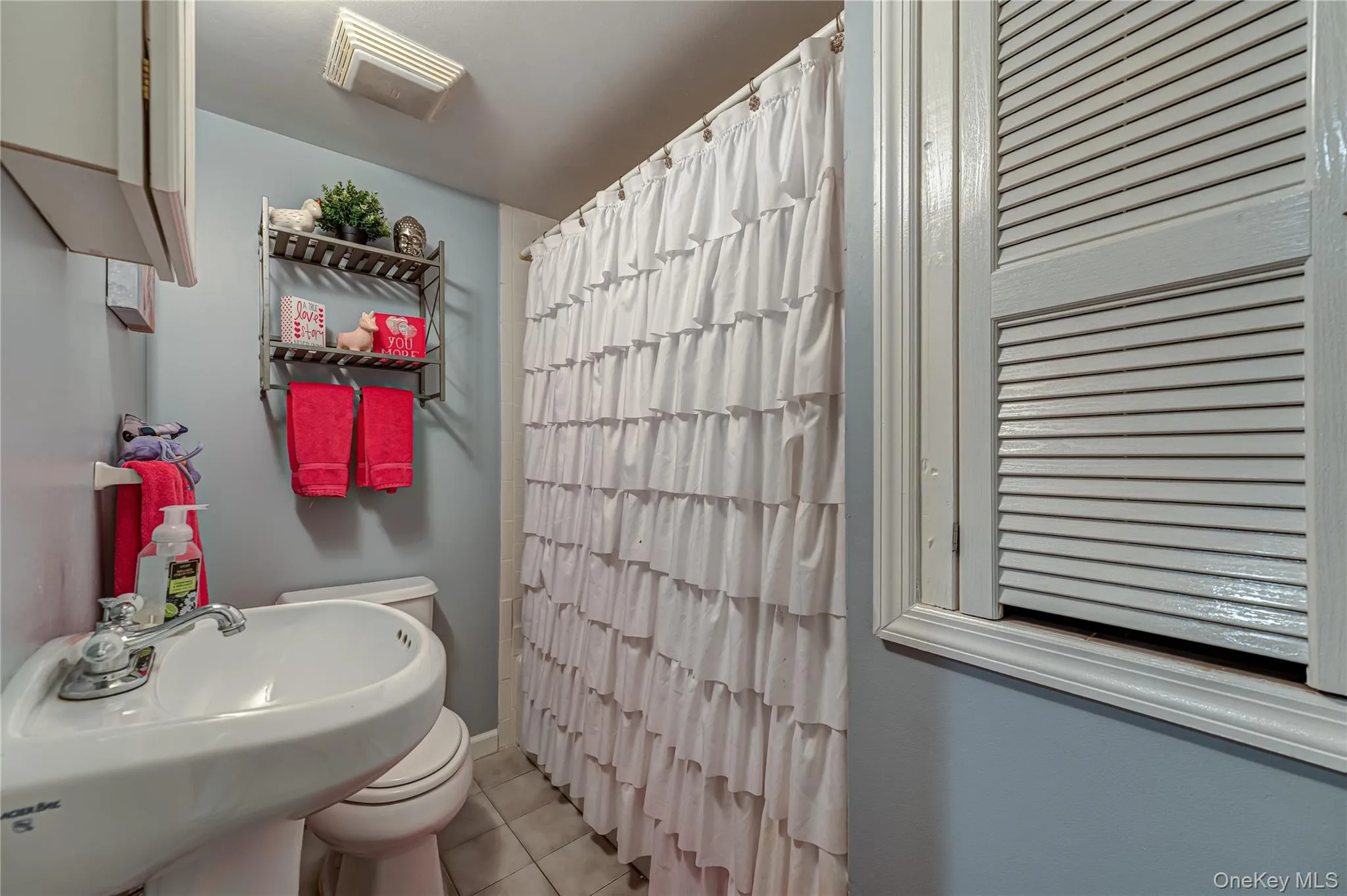 Bathroom featuring a pedestal sink, toilet, and shower with a white ruffled curtain Bathroom featuring a pedestal sink, toilet, and shower with a white ruffled curtain