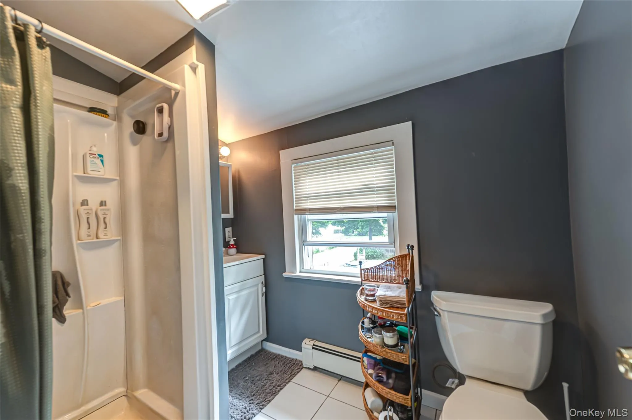 Bathroom featuring a white shower stall with built-in shelving, a single vanity with storage, window and tiled flooring on 2nd floor Bathroom featuring a white shower stall with built-in shelving, a single vanity with storage, window and tiled flooring on 2nd floor