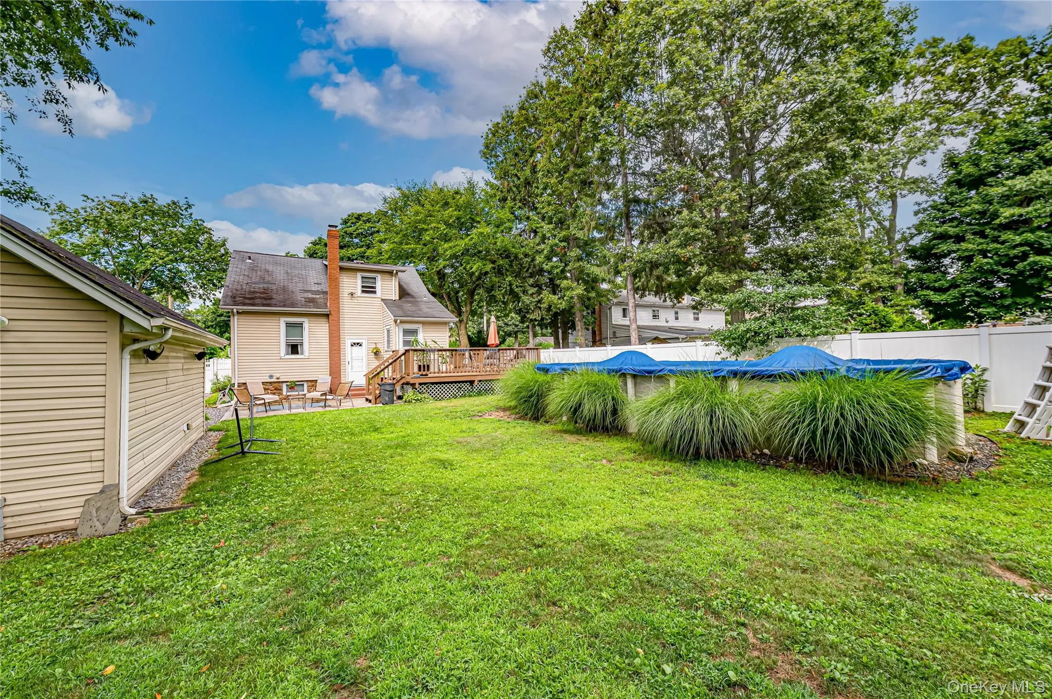 Expansive backyard featuring a covered above-ground pool, a detached garage with vinyl siding, and a rear deck Expansive backyard featuring a covered above-ground pool, a detached garage with vinyl siding, and a rear deck