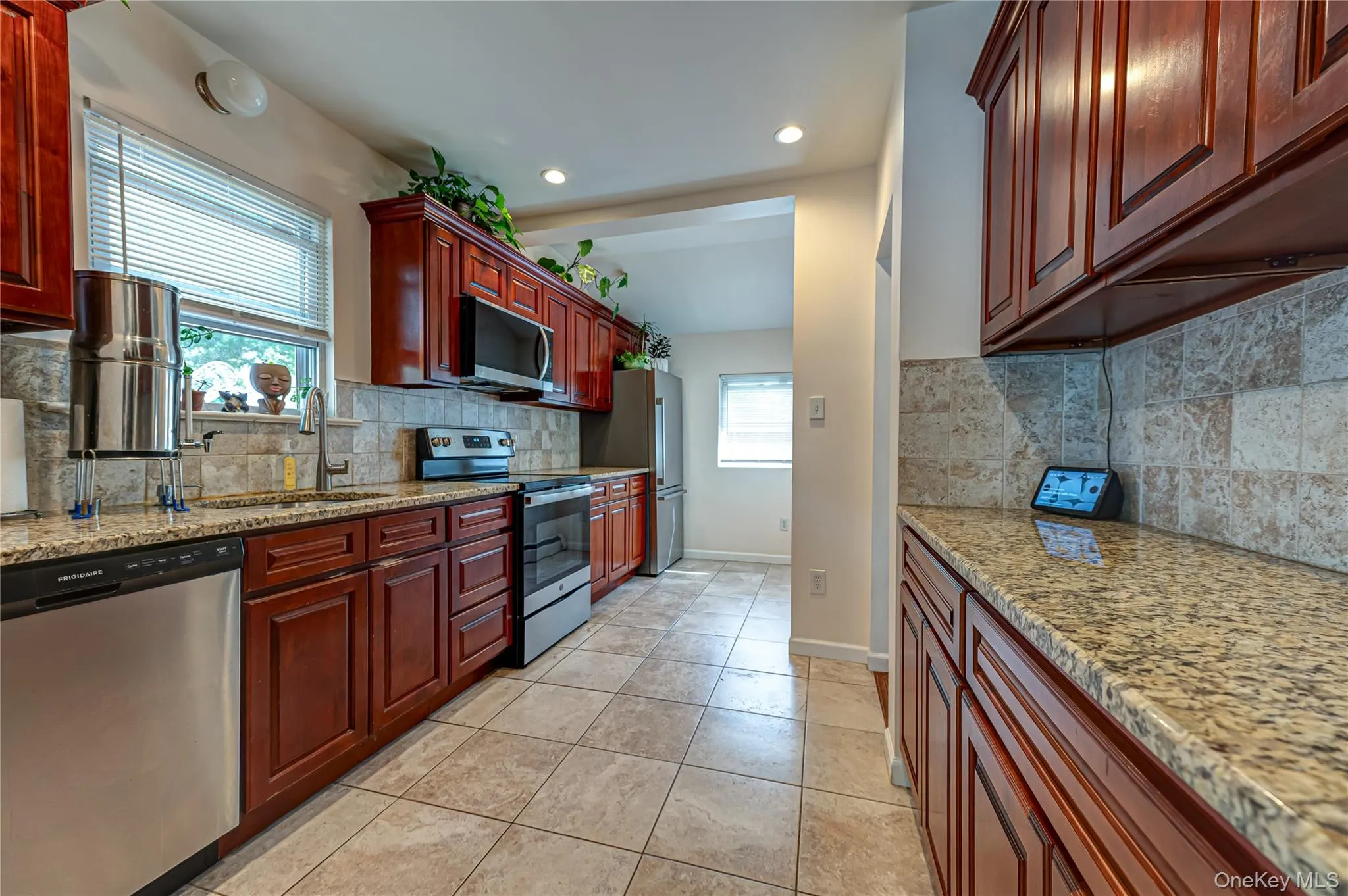 Kitchen featuring rich wood cabinetry, stone countertops, stainless steel appliances, tile flooring, and a tiled backsplash Kitchen featuring rich wood cabinetry, stone countertops, stainless steel appliances, tile flooring, and a tiled backsplash
