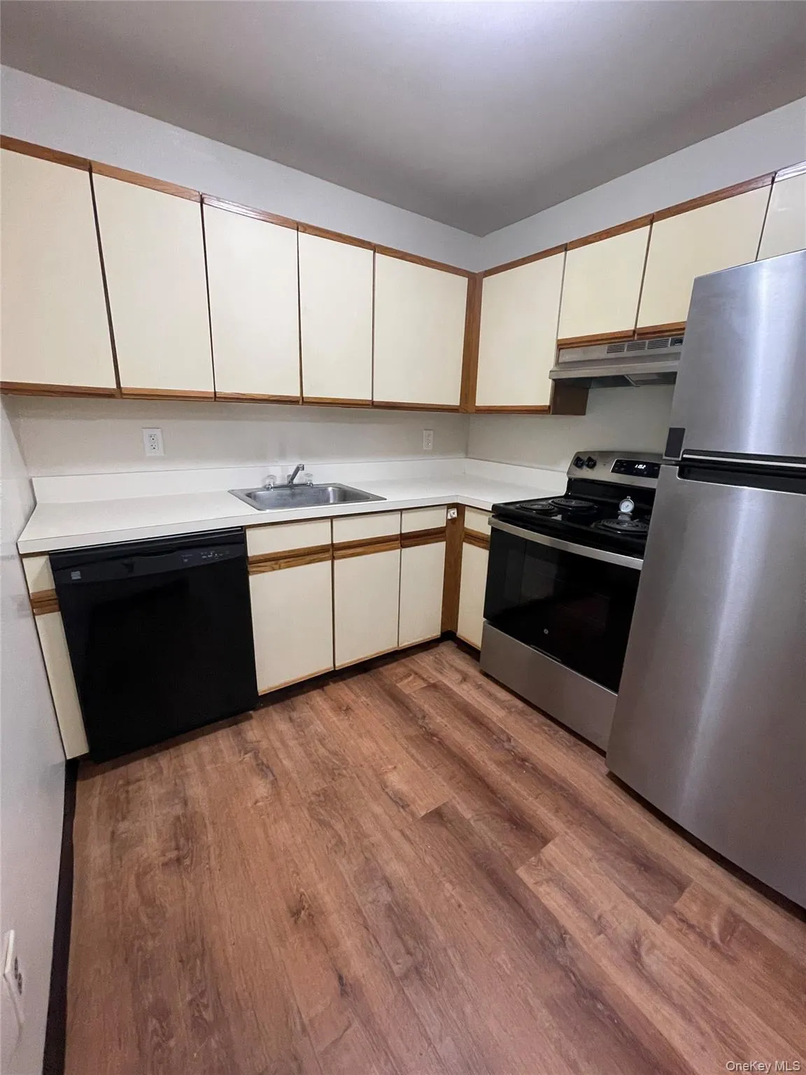 Kitchen featuring wood-finish flooring, white cabinetry with wood trim, stainless steel refrigerator, black/stainless range and black dishwasher Kitchen featuring wood-finish flooring, white cabinetry with wood trim, stainless steel refrigerator, black/stainless range and black dishwasher