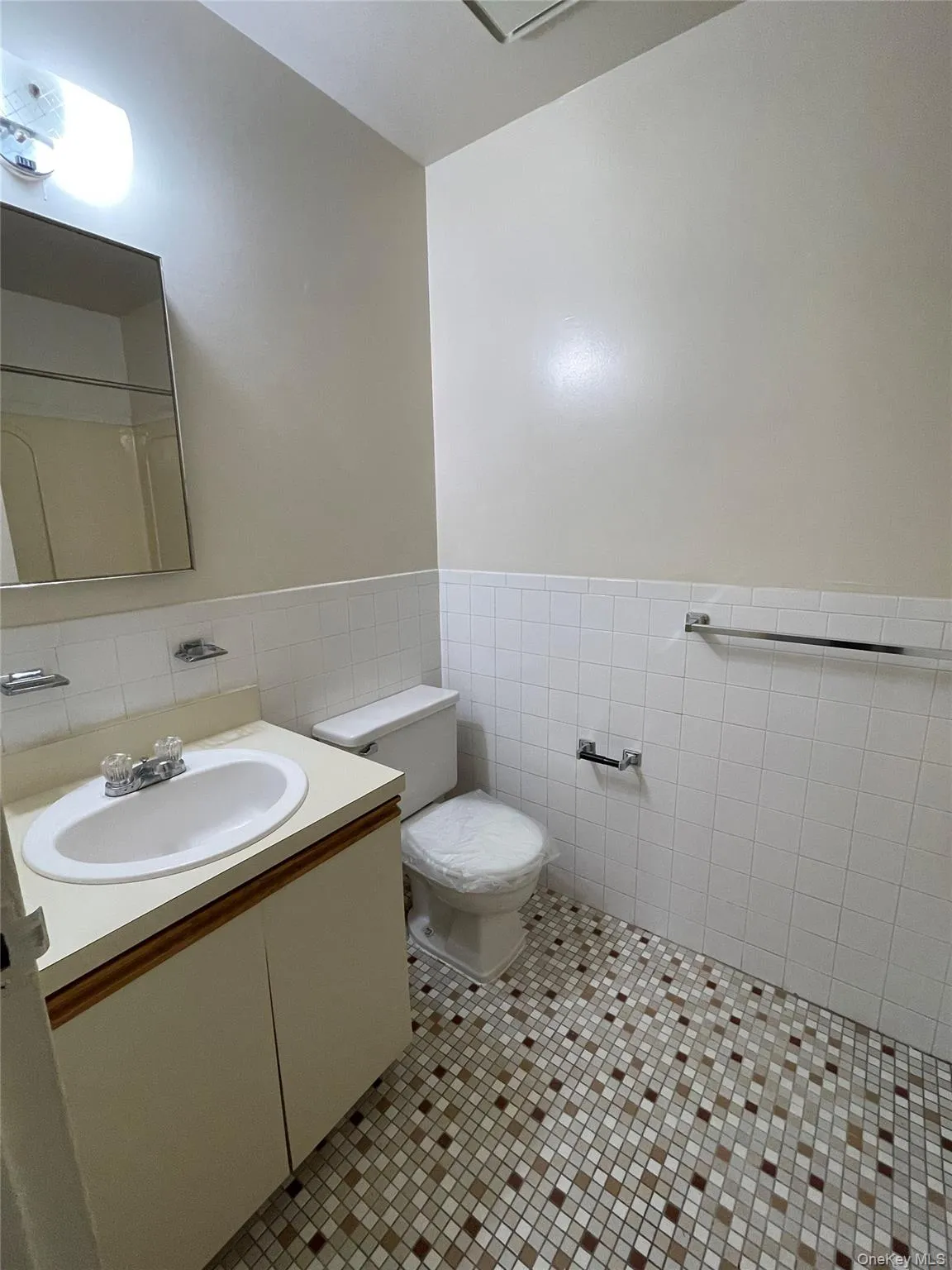 Bathroom featuring mosaic floor tiling, white wall tiling, a vanity with an integrated sink, a mirrored medicine cabinet, and a toilet Bathroom featuring mosaic floor tiling, white wall tiling, a vanity with an integrated sink, a mirrored medicine cabinet, and a toilet