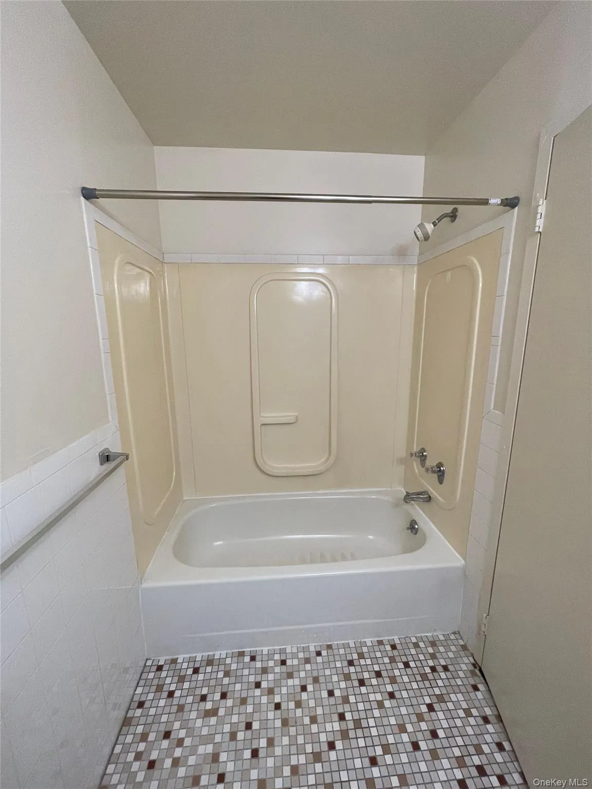 Full-size bathtub with integrated shower, accented by a mosaic tile floor and a wall-mounted towel bar Full-size bathtub with integrated shower, accented by a mosaic tile floor and a wall-mounted towel bar