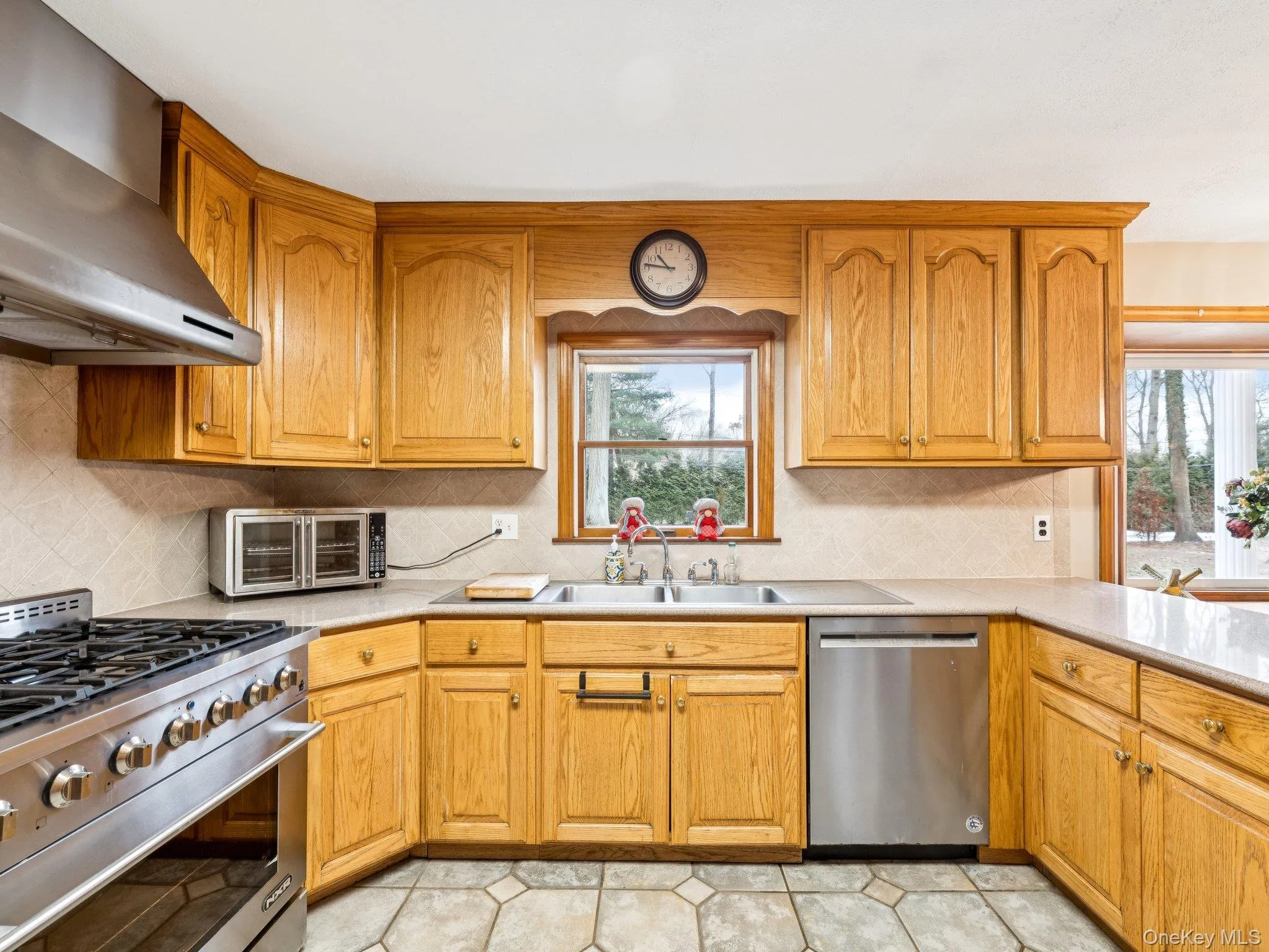 Kitchen with stainless steel appliances, backsplash, wall chimney exhaust hood, and brown cabinetry Kitchen with stainless steel appliances, backsplash, wall chimney exhaust hood, and brown cabinetry