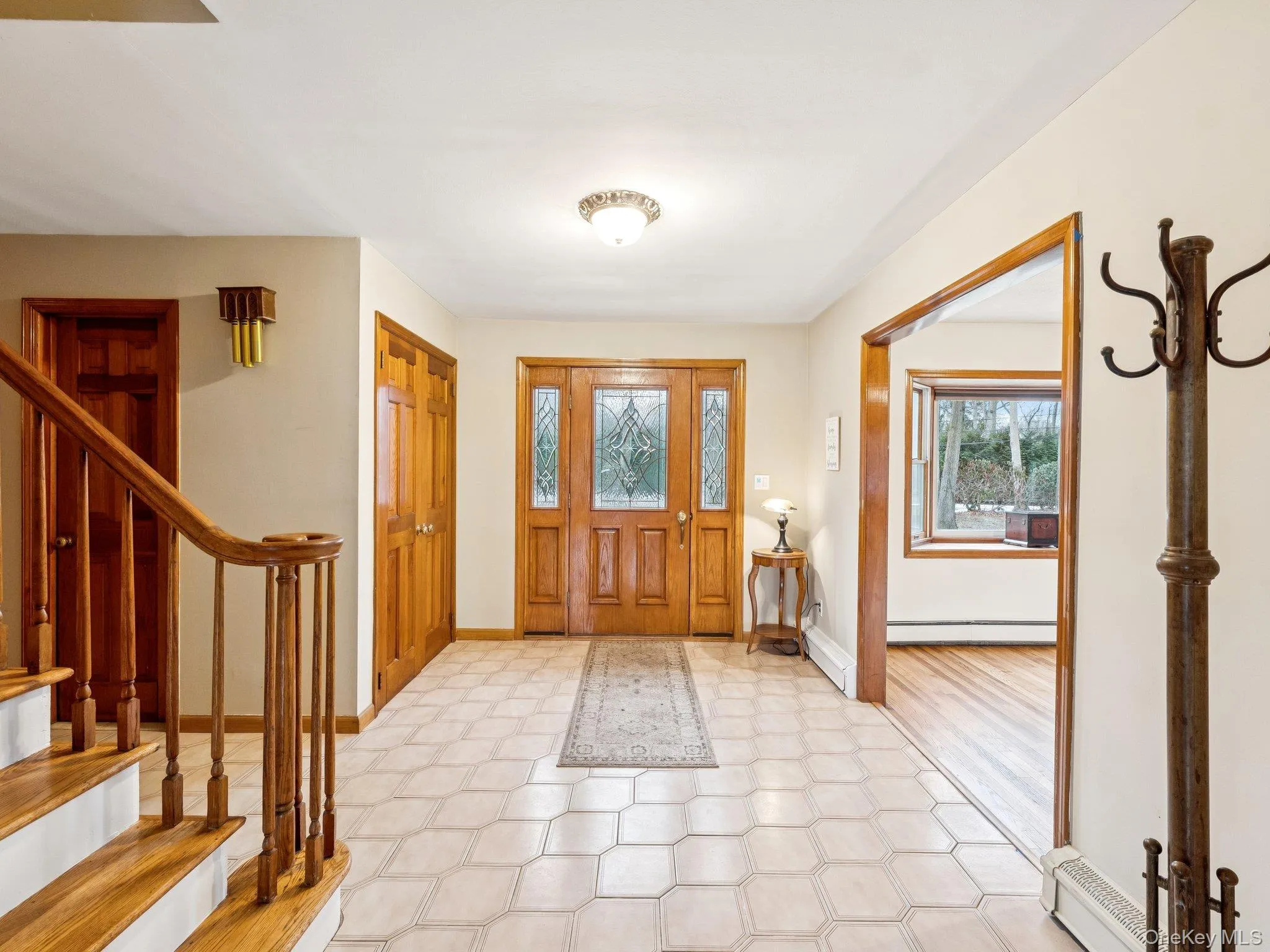 Entrance foyer with light floors, stairway, a baseboard heating unit, and a baseboard radiator Entrance foyer with light floors, stairway, a baseboard heating unit, and a baseboard radiator