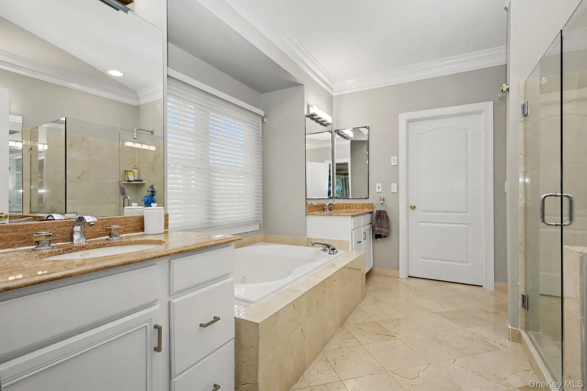 Spacious bathroom featuring dual vanities with stone countertops, a deep soaking tub, a separate glass-enclosed shower, and tile flooring Spacious bathroom featuring dual vanities with stone countertops, a deep soaking tub, a separate glass-enclosed shower, and tile flooring