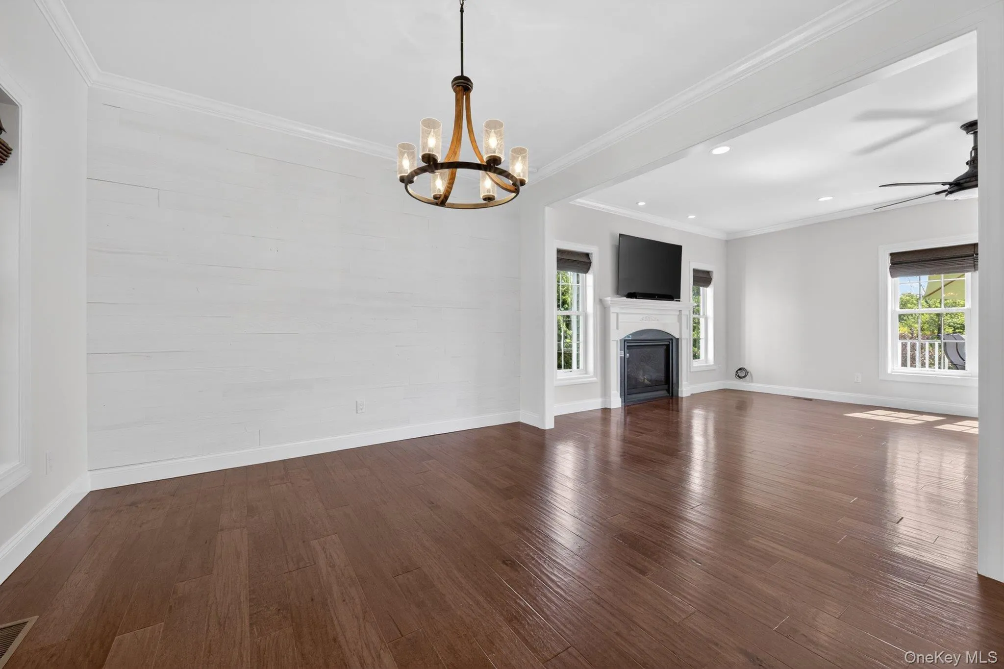 Spacious open-concept living area featuring rich wood-finish flooring, a contemporary chandelier, a white shiplap accent wall, and recessed lighting Spacious open-concept living area featuring rich wood-finish flooring, a contemporary chandelier, a white shiplap accent wall, and recessed lighting