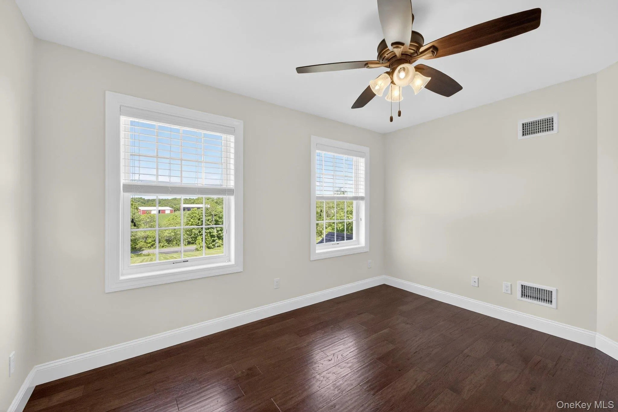 Room featuring dark wood-finish flooring, two windows with white blinds, and a ceiling fan with integrated lighting Room featuring dark wood-finish flooring, two windows with white blinds, and a ceiling fan with integrated lighting