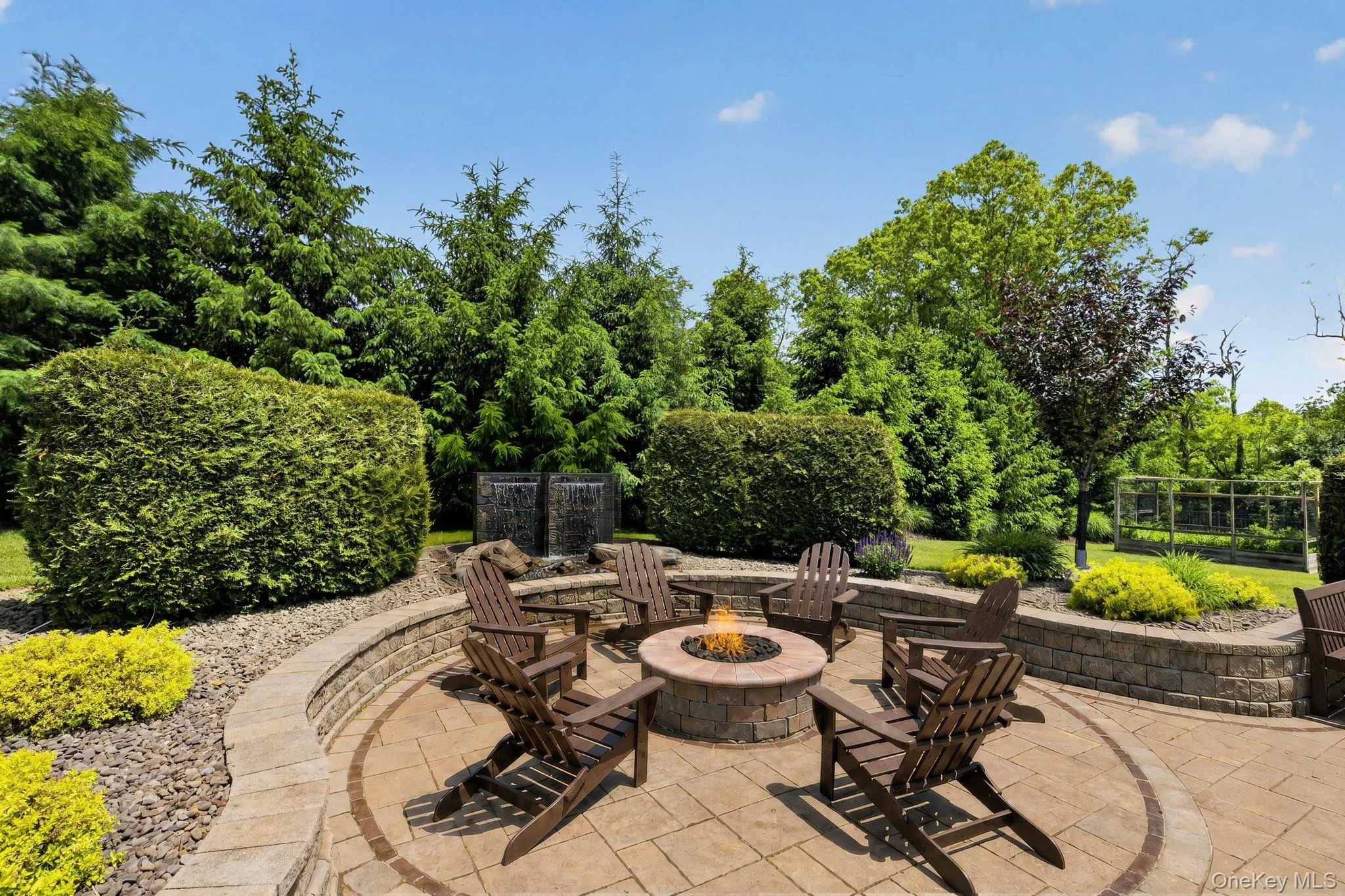Paver patio with an integrated stone fire pit, surrounded by tiered landscaping, mature trees, and a dual waterfall feature Paver patio with an integrated stone fire pit, surrounded by tiered landscaping, mature trees, and a dual waterfall feature