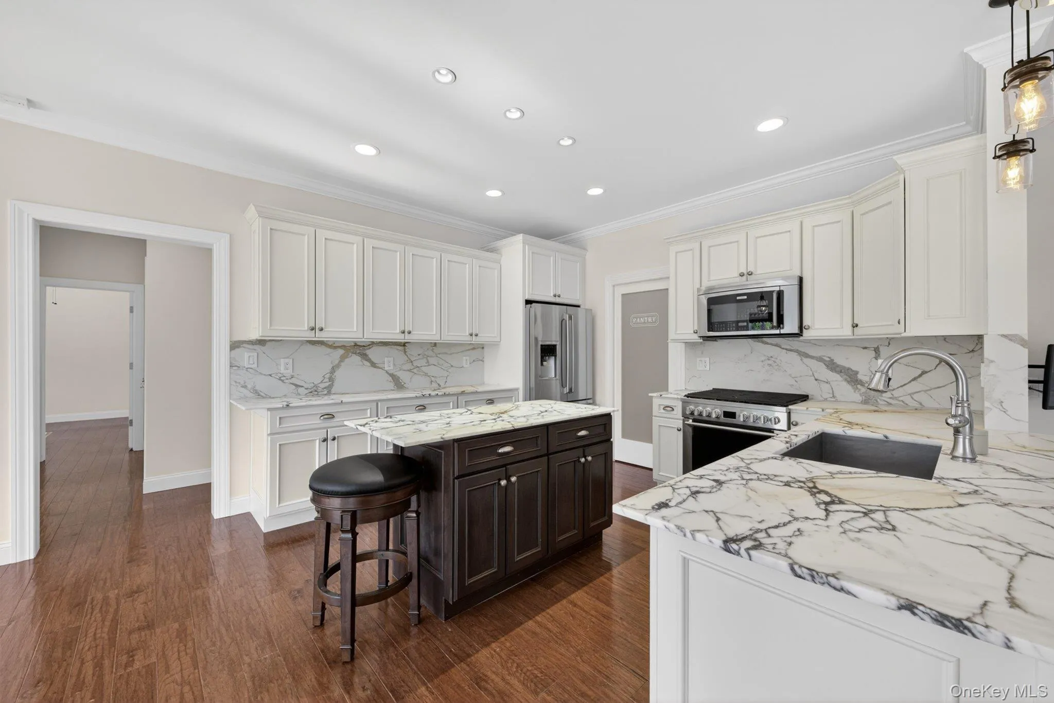 Kitchen featuring white cabinetry, a dark wood-finish island with storage, stainless steel appliances, marble-look countertops and backsplash, and recessed lighting Kitchen featuring white cabinetry, a dark wood-finish island with storage, stainless steel appliances, marble-look countertops and backsplash, and recessed lighting