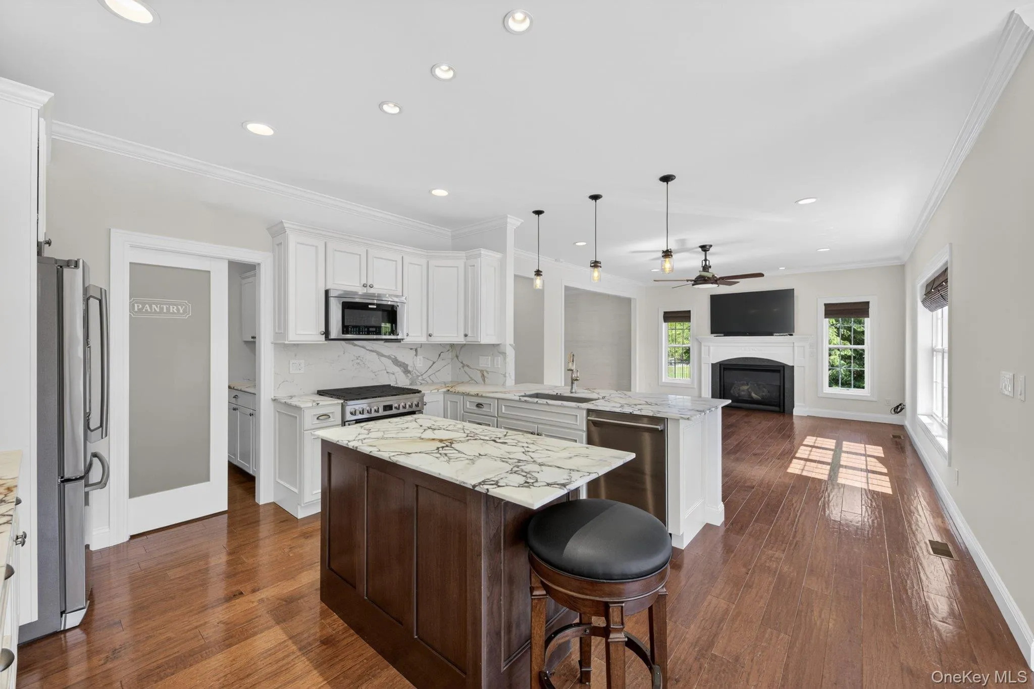 Open-concept kitchen featuring an island with seating, white shaker cabinetry, stainless steel appliances, and wood-finish flooring Open-concept kitchen featuring an island with seating, white shaker cabinetry, stainless steel appliances, and wood-finish flooring