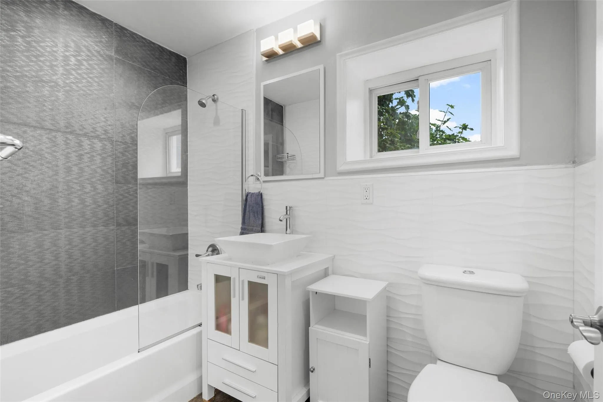 Bathroom featuring a white vanity with vessel sink, a shower-over-tub combination with glass partition. Bathroom featuring a white vanity with vessel sink, a shower-over-tub combination with glass partition.
