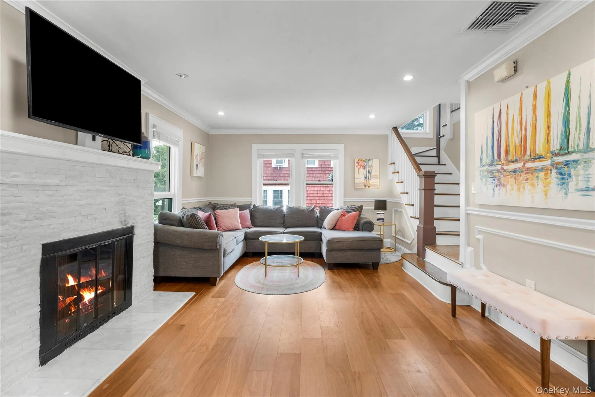 Spacious interior featuring wood-finish flooring, a white stacked stone fireplace, and crown molding, recessed lighting. Spacious interior featuring wood-finish flooring, a white stacked stone fireplace, and crown molding, recessed lighting.