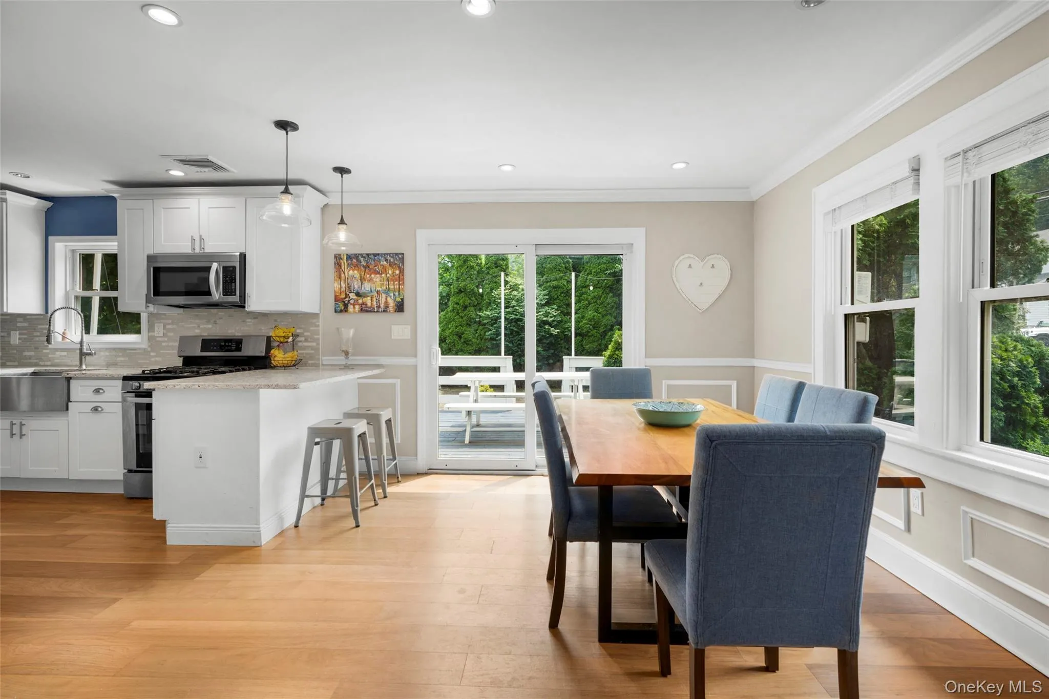 Open-concept kitchen and dining area featuring light wood-finish flooring, white cabinetry, stainless steel appliances, and sliding glass doors to outdoor space. Open-concept kitchen and dining area featuring light wood-finish flooring, white cabinetry, stainless steel appliances, and sliding glass doors to outdoor space.