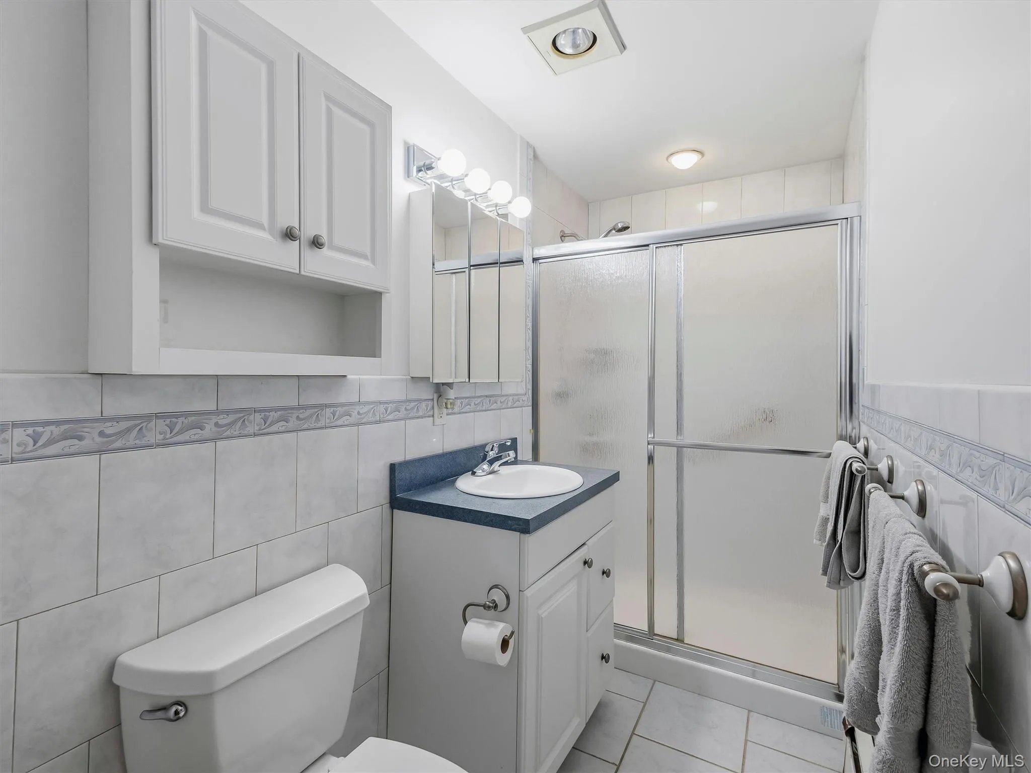Full Guest bathroom featuring a white vanity with a blue countertop, a shower with a sliding glass door, tiled walls with a decorative border. Full Guest bathroom featuring a white vanity with a blue countertop, a shower with a sliding glass door, tiled walls with a decorative border.