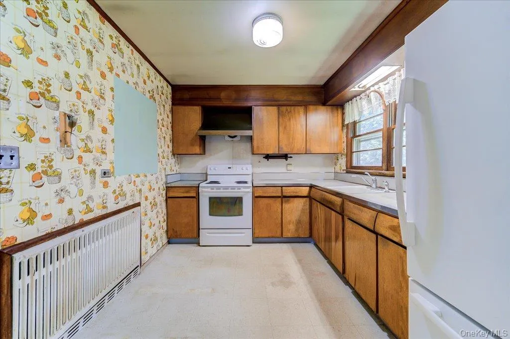 Kitchen featuring wood cabinetry, white appliances, a window above the sink, and a radiator Kitchen featuring wood cabinetry, white appliances, a window above the sink, and a radiator