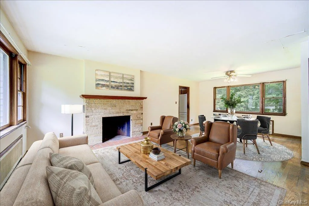 Living area virtually staged)(featuring a stone-clad fireplace with a wood mantel, wood-finish flooring, multiple large windows, and a ceiling fan with integrated lighting Living area virtually staged)(featuring a stone-clad fireplace with a wood mantel, wood-finish flooring, multiple large windows, and a ceiling fan with integrated lighting