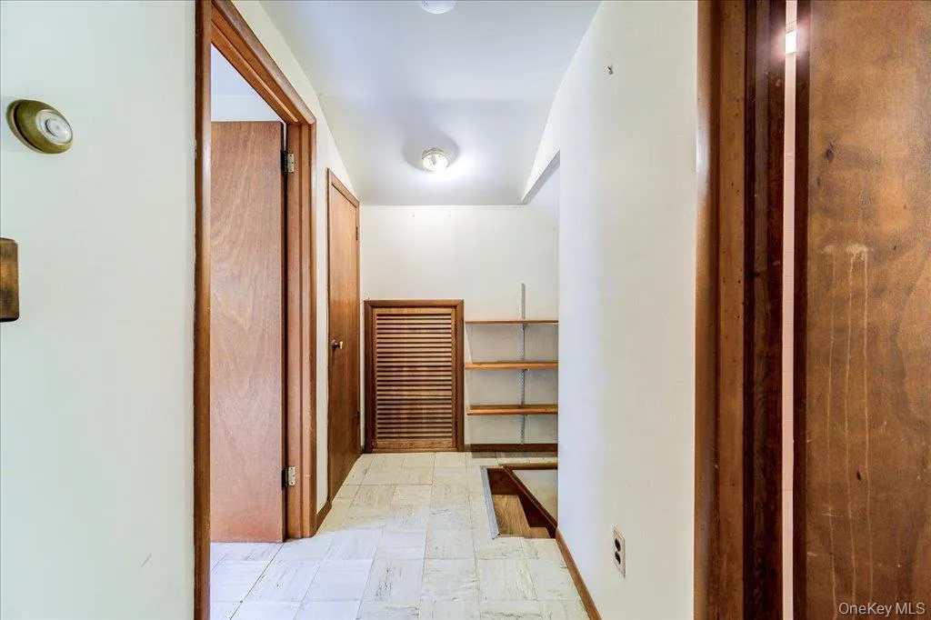 Hallway featuring a louvered door, built-in shelving, and wood-finish doors and trim Hallway featuring a louvered door, built-in shelving, and wood-finish doors and trim