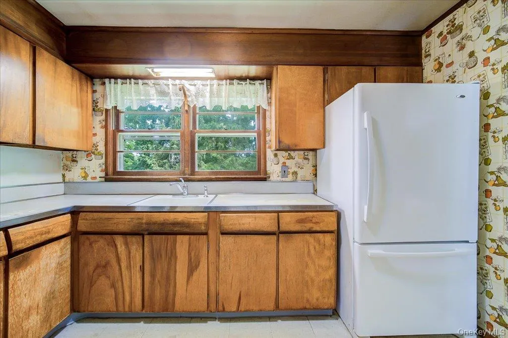 Galley kitchen featuring wood cabinetry, a double basin stainless steel sink, and a white refrigerator Galley kitchen featuring wood cabinetry, a double basin stainless steel sink, and a white refrigerator