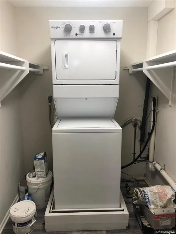 Dedicated laundry closet with stacked washer and dryer, built-in shelving, and wood-finish flooring Dedicated laundry closet with stacked washer and dryer, built-in shelving, and wood-finish flooring
