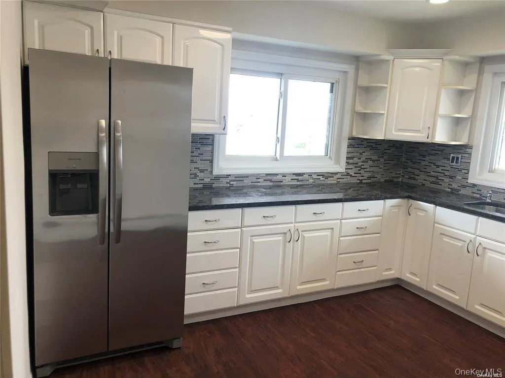 Kitchen featuring white cabinetry, dark stone countertops, a mosaic tile backsplash, and wood-finish flooring Kitchen featuring white cabinetry, dark stone countertops, a mosaic tile backsplash, and wood-finish flooring