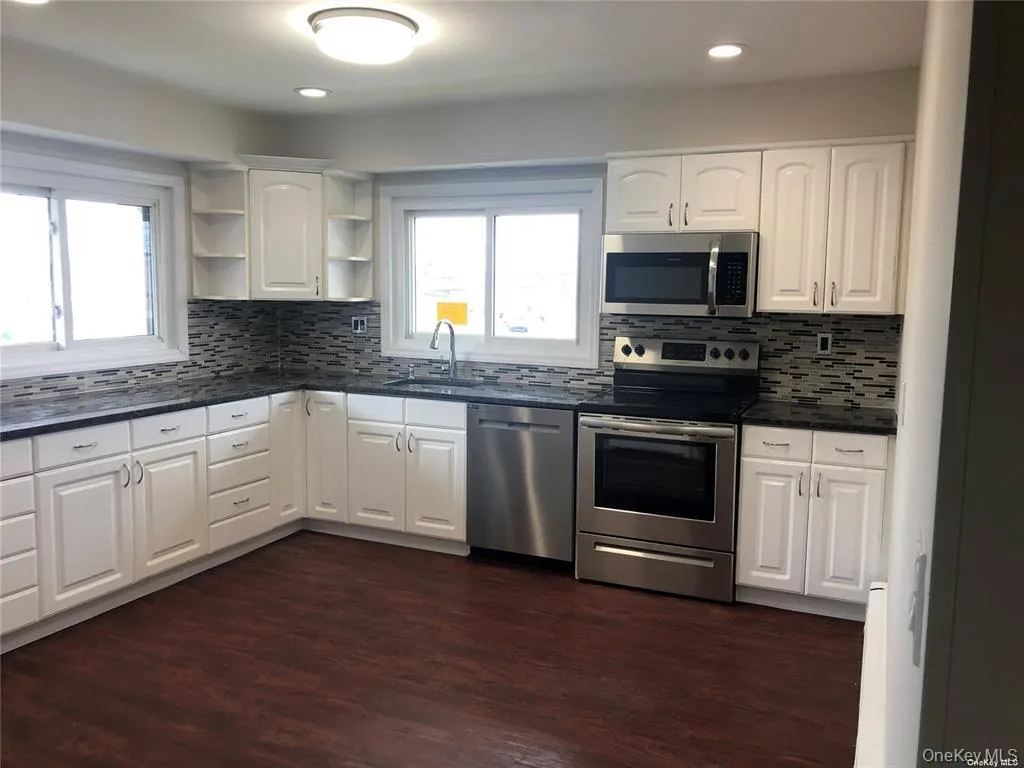 Modern kitchen featuring white cabinetry, dark countertops, and a mosaic tile backsplash Modern kitchen featuring white cabinetry, dark countertops, and a mosaic tile backsplash