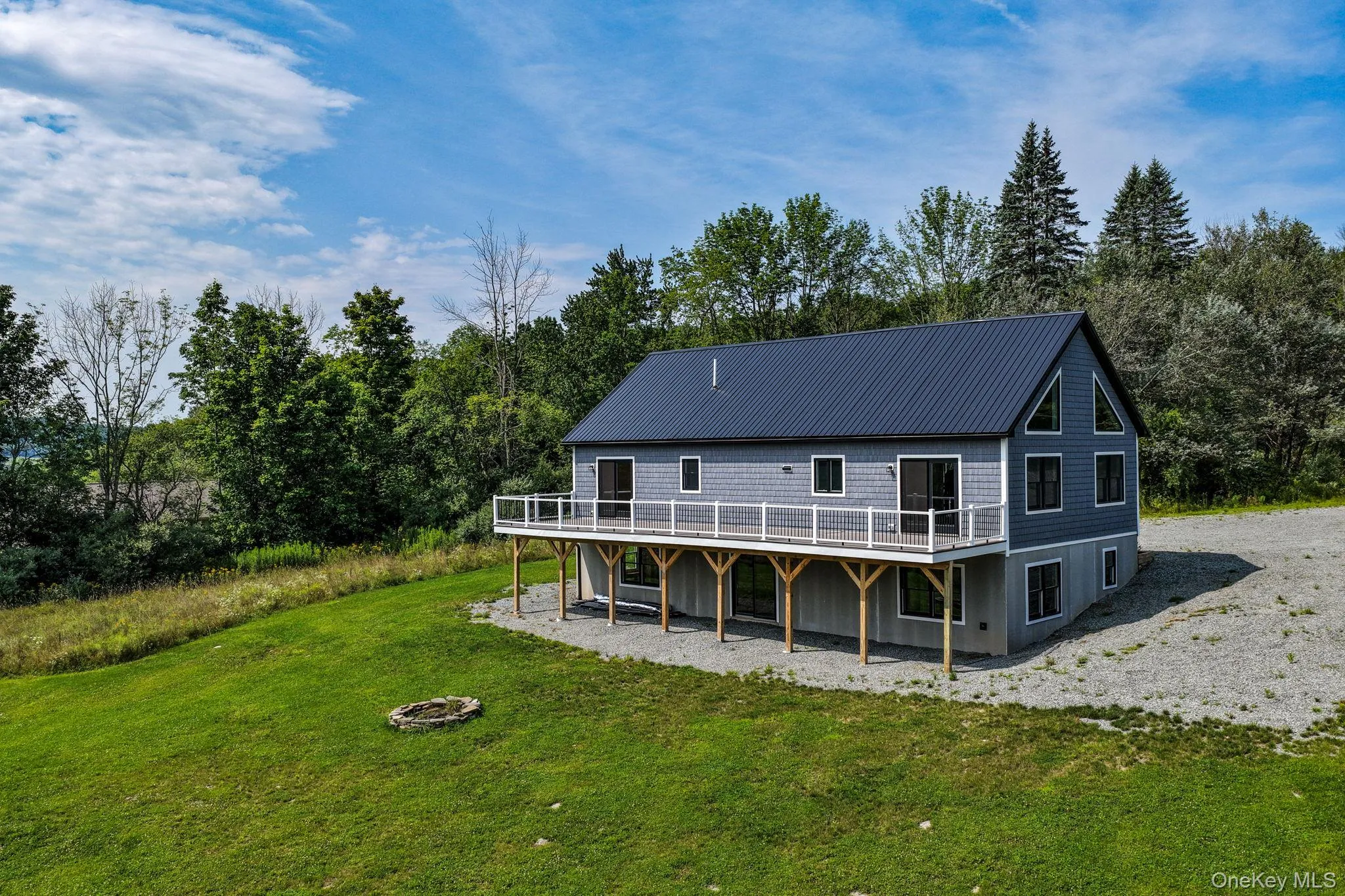 Modern farmhouse featuring a dark metal roof, horizontal wood-finish siding, and a wraparound deck with wood railings Modern farmhouse featuring a dark metal roof, horizontal wood-finish siding, and a wraparound deck with wood railings