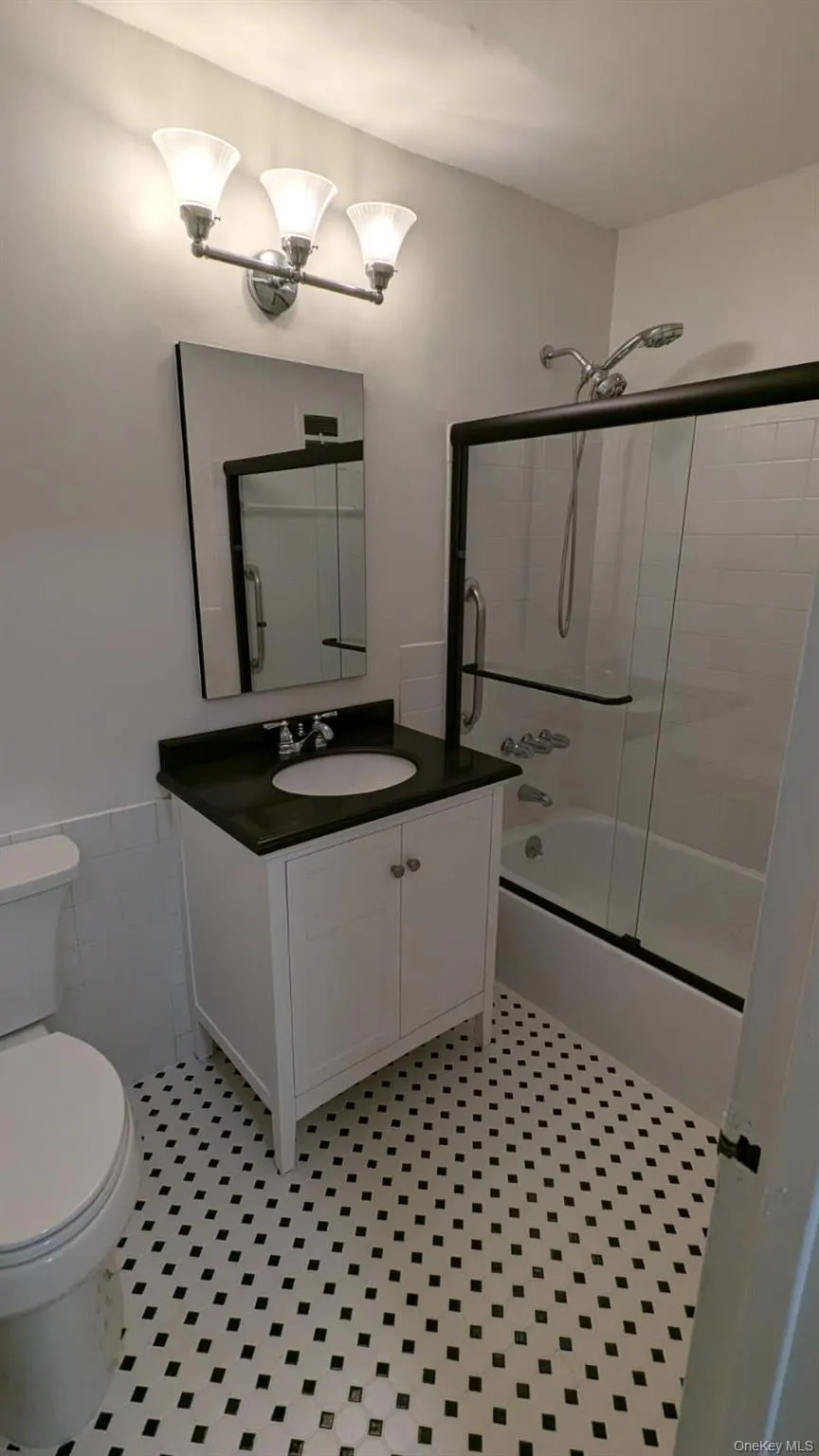 Full bathroom with vanity, toilet, tile patterned floors, and bath / shower combo with glass door Full bathroom with vanity, toilet, tile patterned floors, and bath / shower combo with glass door