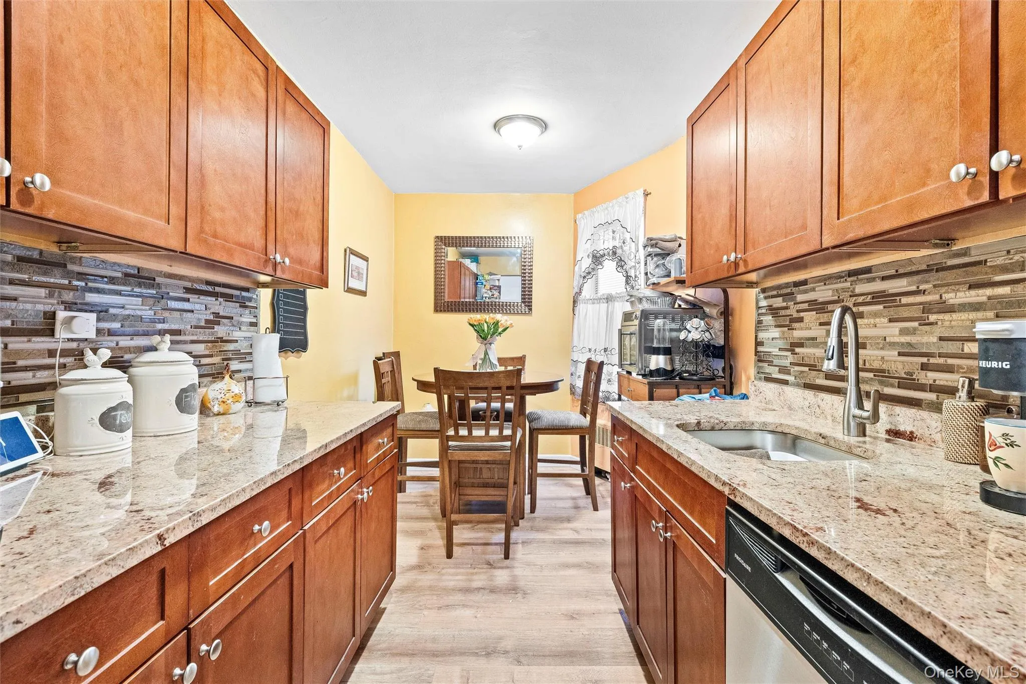 Kitchen with light wood-type flooring, decorative backsplash, a sink, and dishwasher Kitchen with light wood-type flooring, decorative backsplash, a sink, and dishwasher