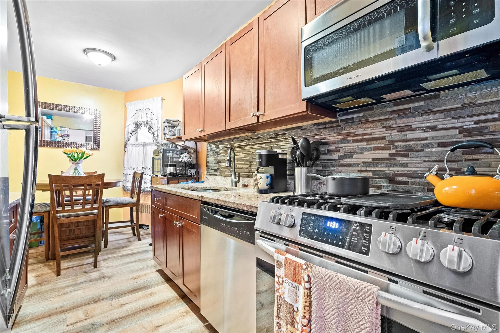 Kitchen featuring a sink, brown cabinetry, light wood-style flooring, stainless steel appliances, and decorative backsplash Kitchen featuring a sink, brown cabinetry, light wood-style flooring, stainless steel appliances, and decorative backsplash