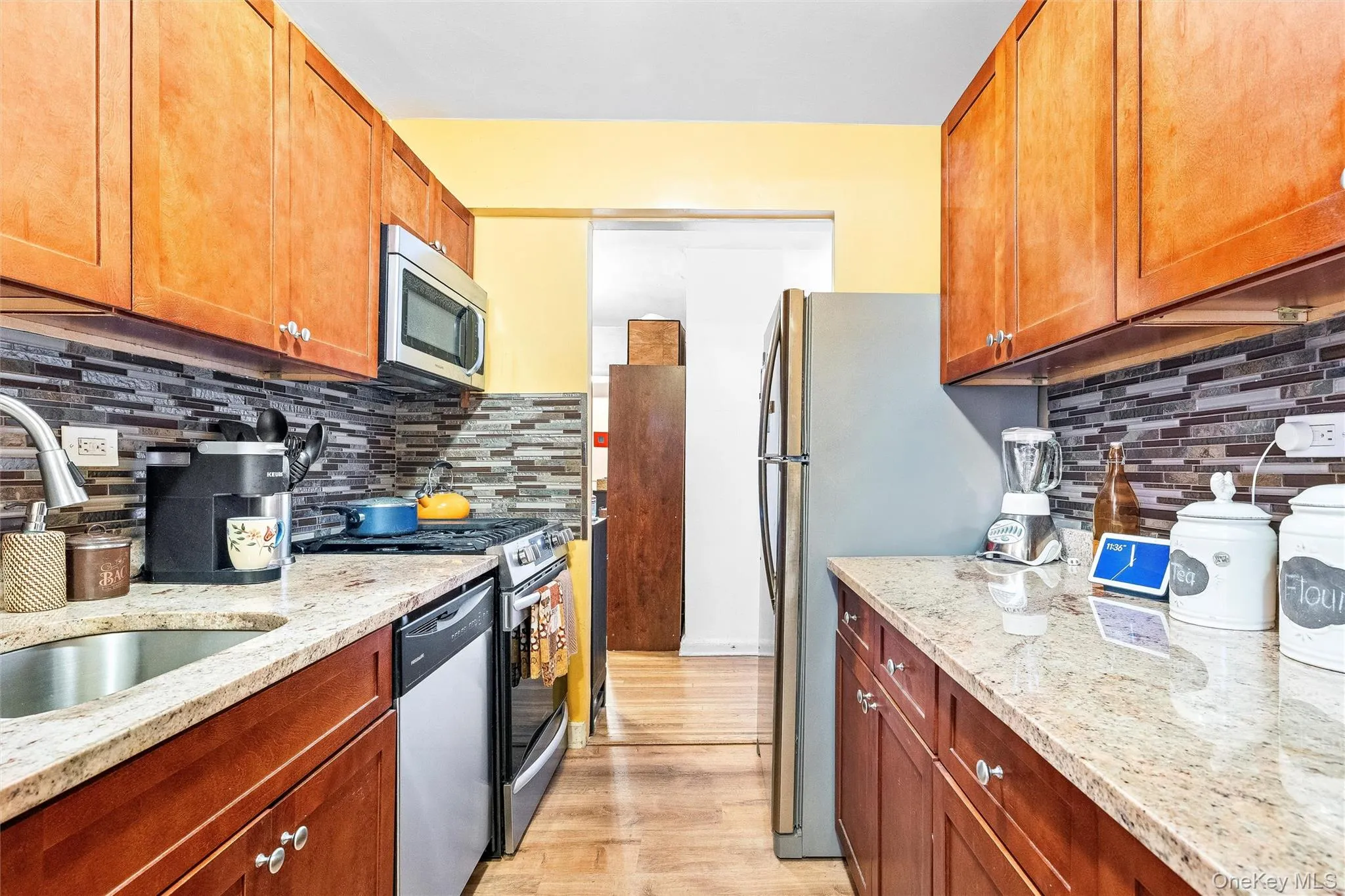 Kitchen featuring backsplash, a sink, light stone counters, stainless steel appliances, and light wood-style flooring Kitchen featuring backsplash, a sink, light stone counters, stainless steel appliances, and light wood-style flooring