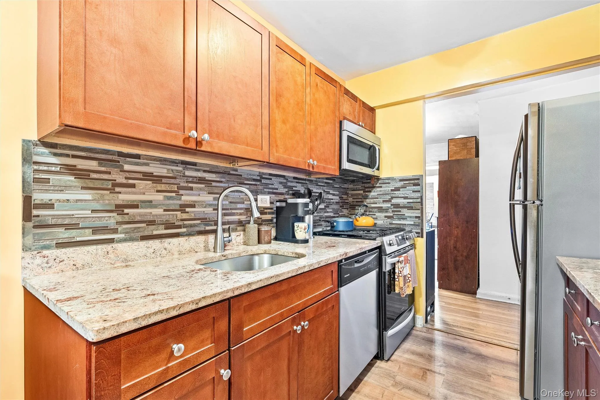 Kitchen featuring appliances with stainless steel finishes, decorative backsplash, a sink, and light wood-type flooring Kitchen featuring appliances with stainless steel finishes, decorative backsplash, a sink, and light wood-type flooring