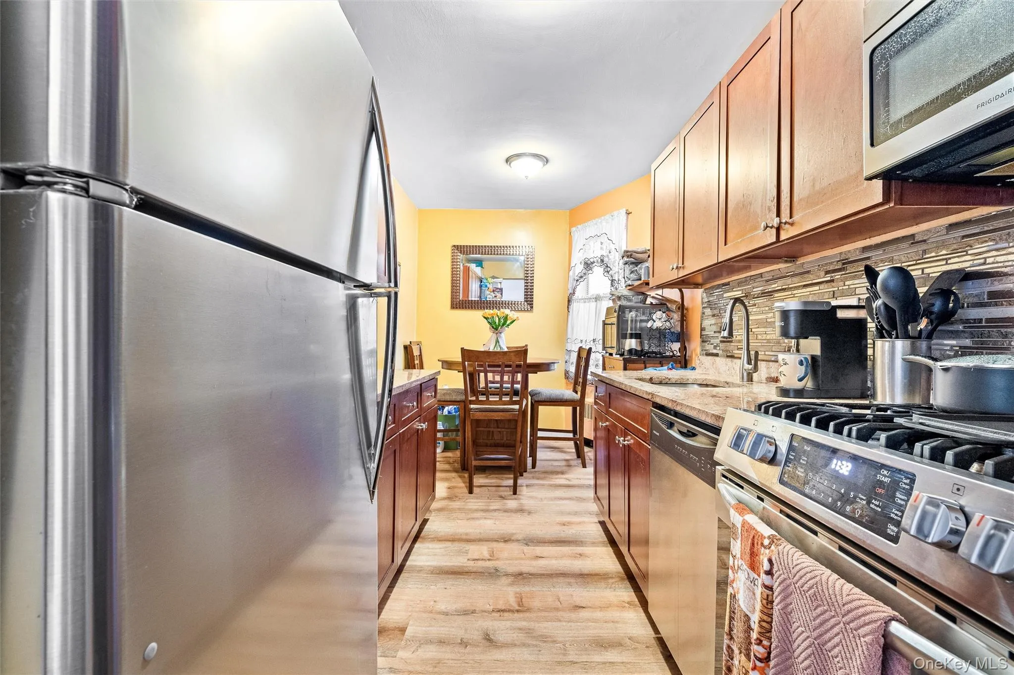 Kitchen featuring appliances with stainless steel finishes, light stone counters, a sink, light wood-style flooring, and backsplash Kitchen featuring appliances with stainless steel finishes, light stone counters, a sink, light wood-style flooring, and backsplash