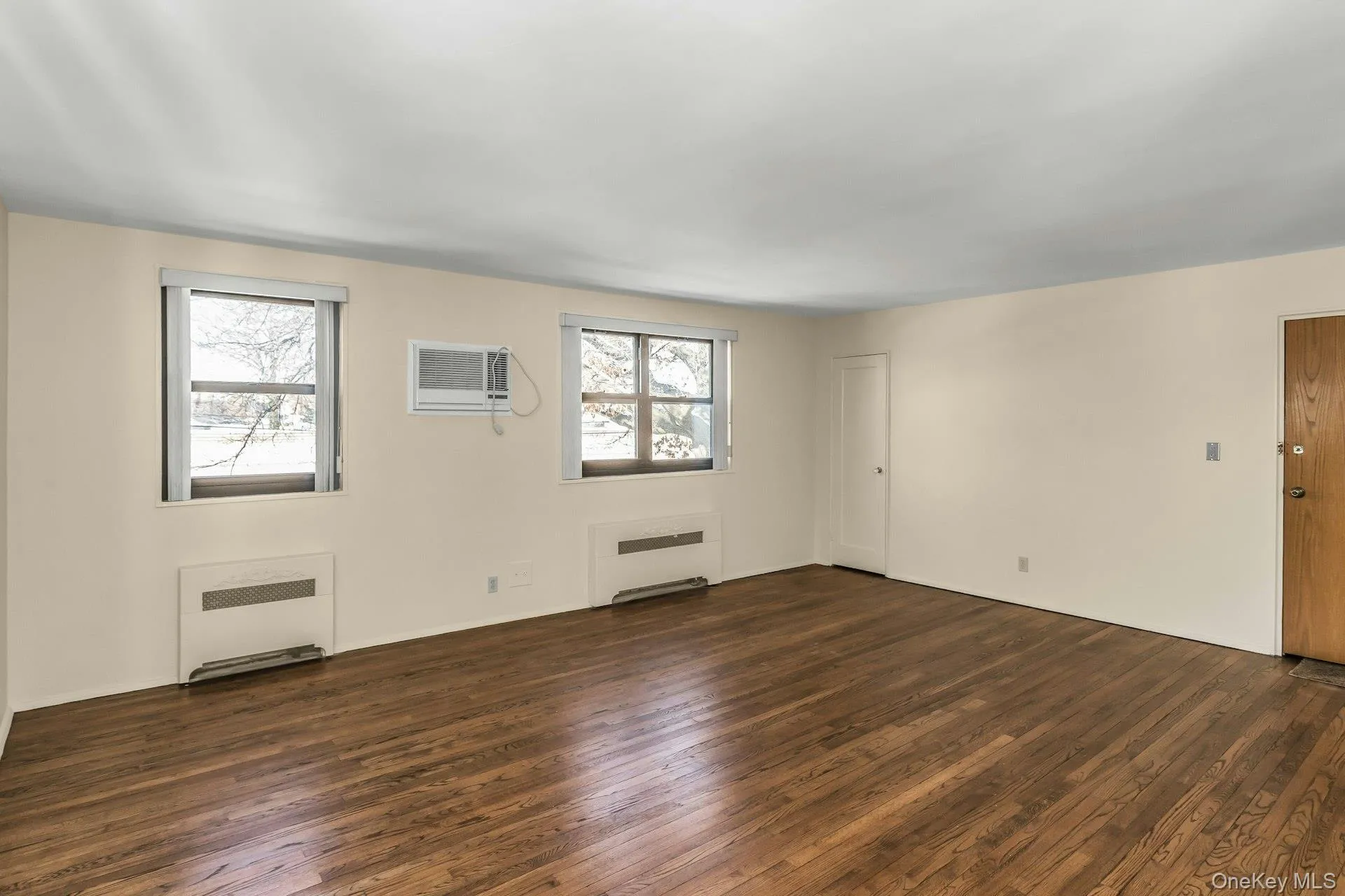 Unfurnished living room featuring radiator, dark wood-style floors, and a wall unit AC Unfurnished living room featuring radiator, dark wood-style floors, and a wall unit AC