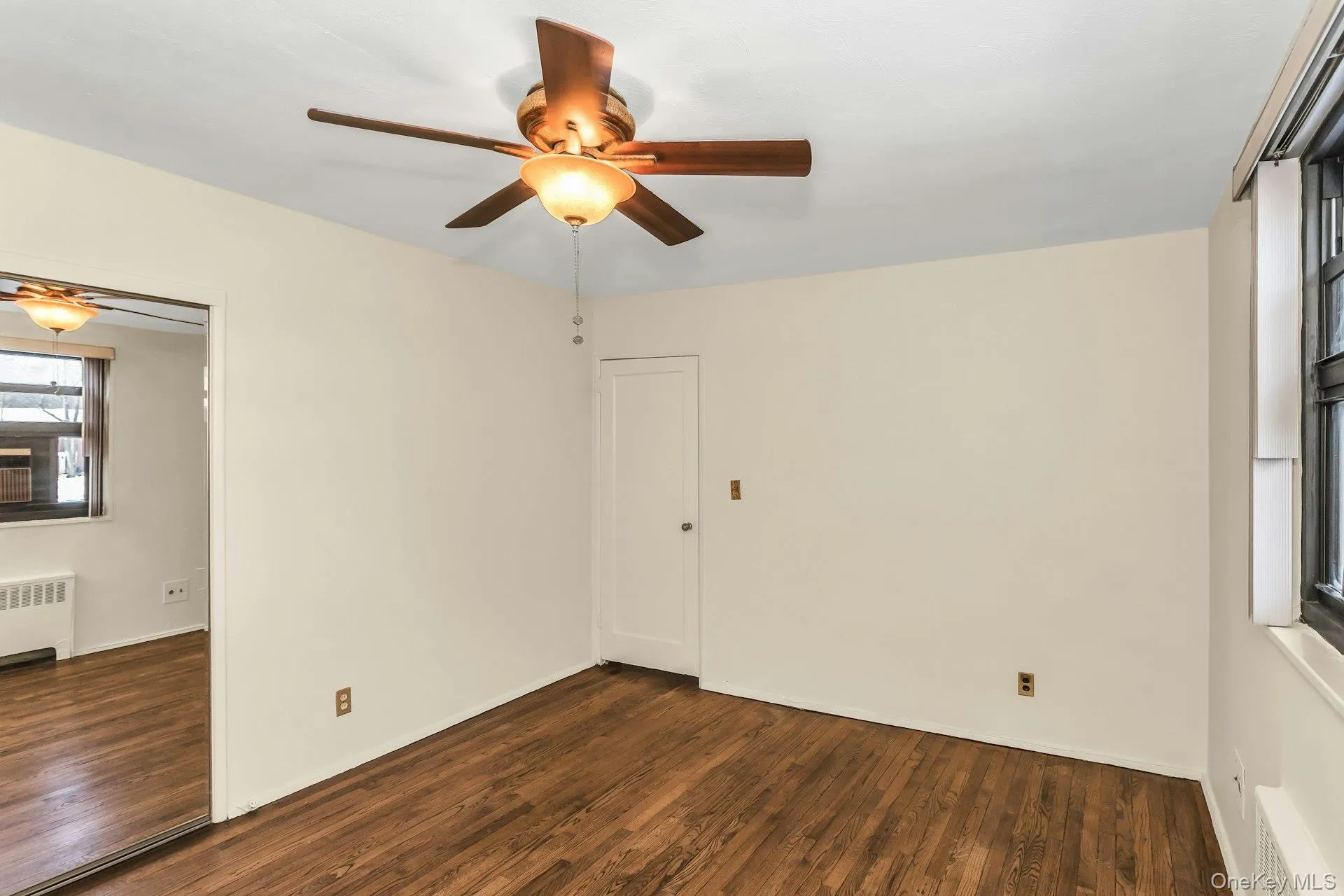 Empty room featuring dark wood finished floors, ceiling fan, and radiator heating unit Empty room featuring dark wood finished floors, ceiling fan, and radiator heating unit