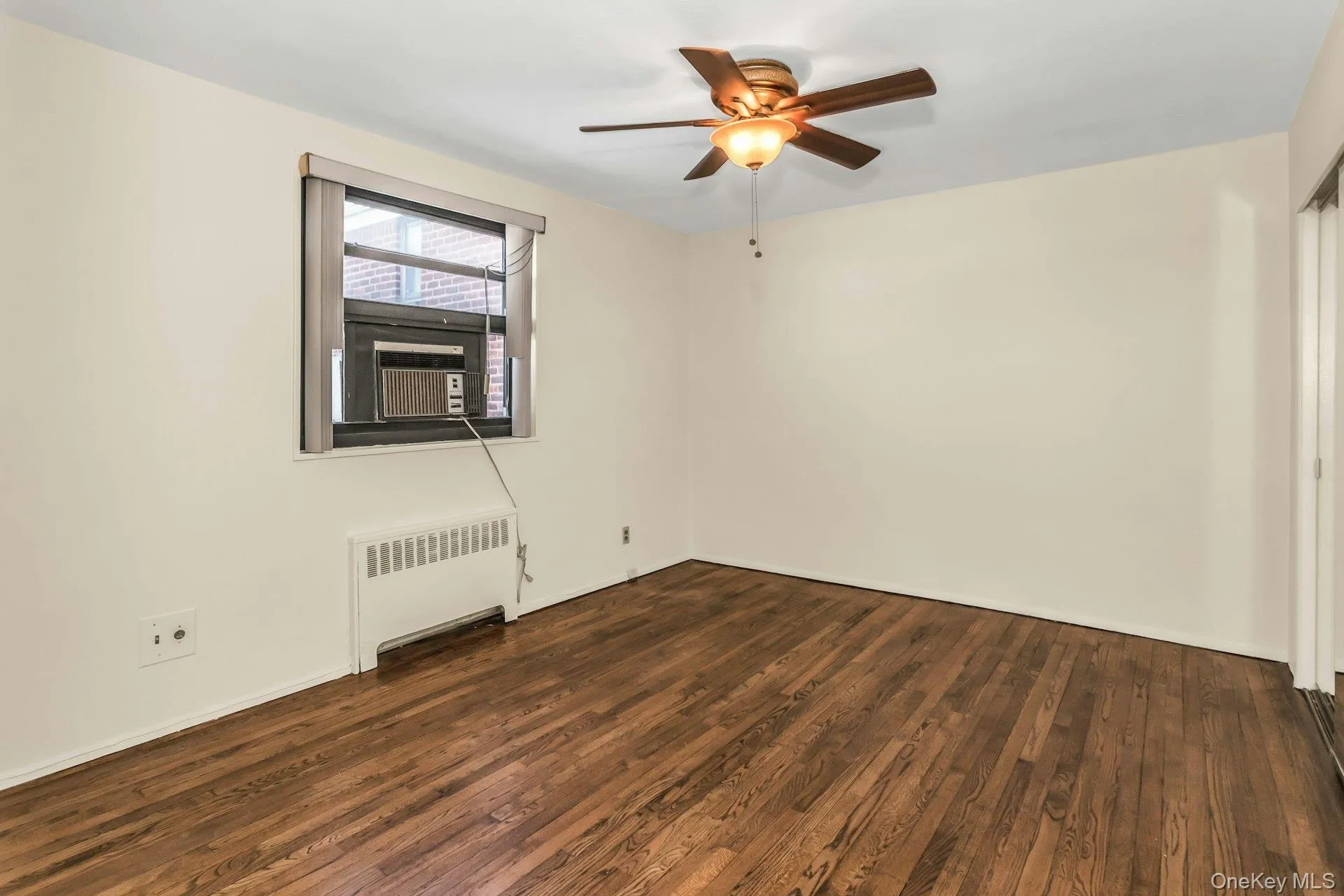 Empty room featuring radiator, dark wood finished floors, and ceiling fan Empty room featuring radiator, dark wood finished floors, and ceiling fan