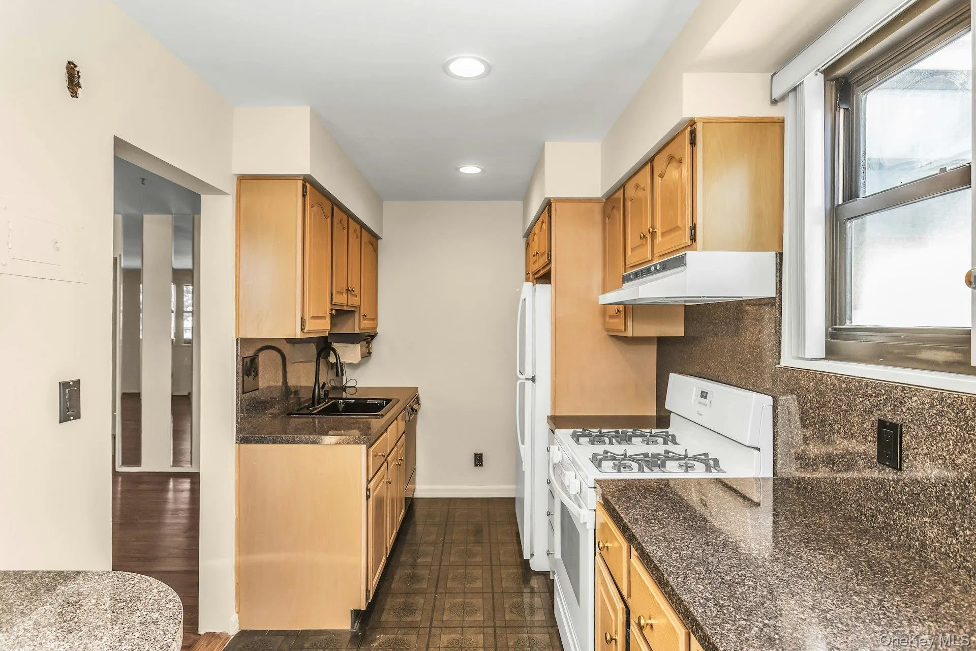 Kitchen with white appliances, under cabinet range hood, recessed lighting, dark stone countertops, and backsplash Kitchen with white appliances, under cabinet range hood, recessed lighting, dark stone countertops, and backsplash