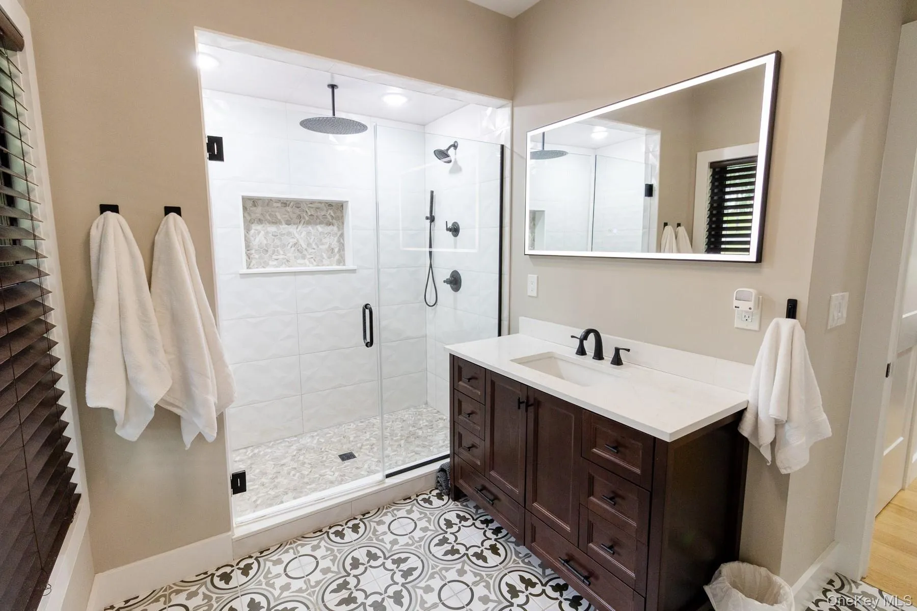 A frameless glass shower, striking patterned tile flooring, and rich vanity cabinetry combine to create a primary bathroom with timeless character and thoughtful attention to detail. A frameless glass shower, striking patterned tile flooring, and rich vanity cabinetry combine to create a primary bathroom with timeless character and thoughtful attention to detail.