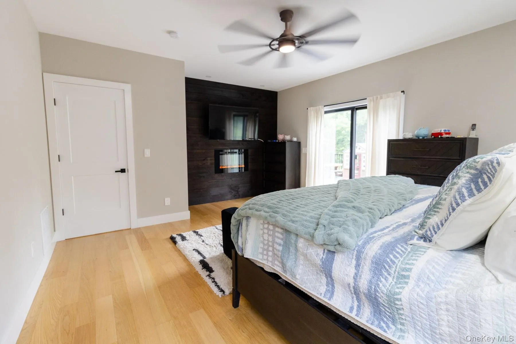 A striking accent wall with integrated fireplace in the primary bedroom creates a distinct focal point, while sliding doors invite natural light and easy outdoor access. A striking accent wall with integrated fireplace in the primary bedroom creates a distinct focal point, while sliding doors invite natural light and easy outdoor access.