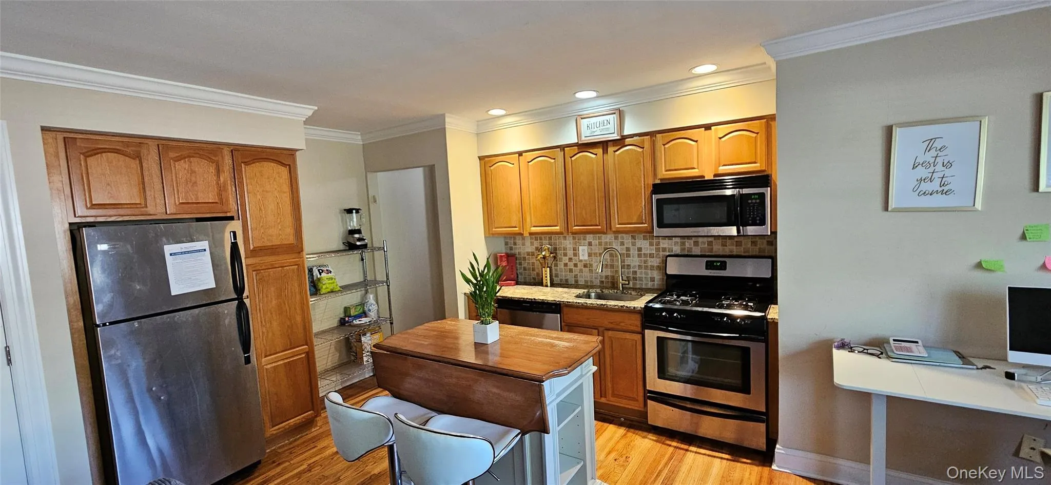 Kitchen with stainless steel appliances, light wood finished floors, ornamental molding, decorative backsplash, and brown cabinets Kitchen with stainless steel appliances, light wood finished floors, ornamental molding, decorative backsplash, and brown cabinets