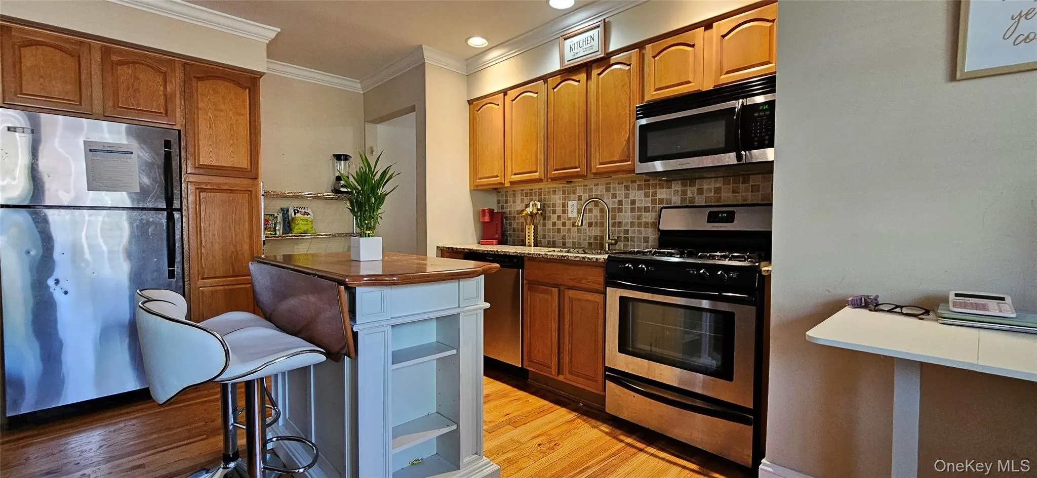 Kitchen featuring appliances with stainless steel finishes, light wood finished floors, ornamental molding, decorative backsplash, and brown cabinets Kitchen featuring appliances with stainless steel finishes, light wood finished floors, ornamental molding, decorative backsplash, and brown cabinets