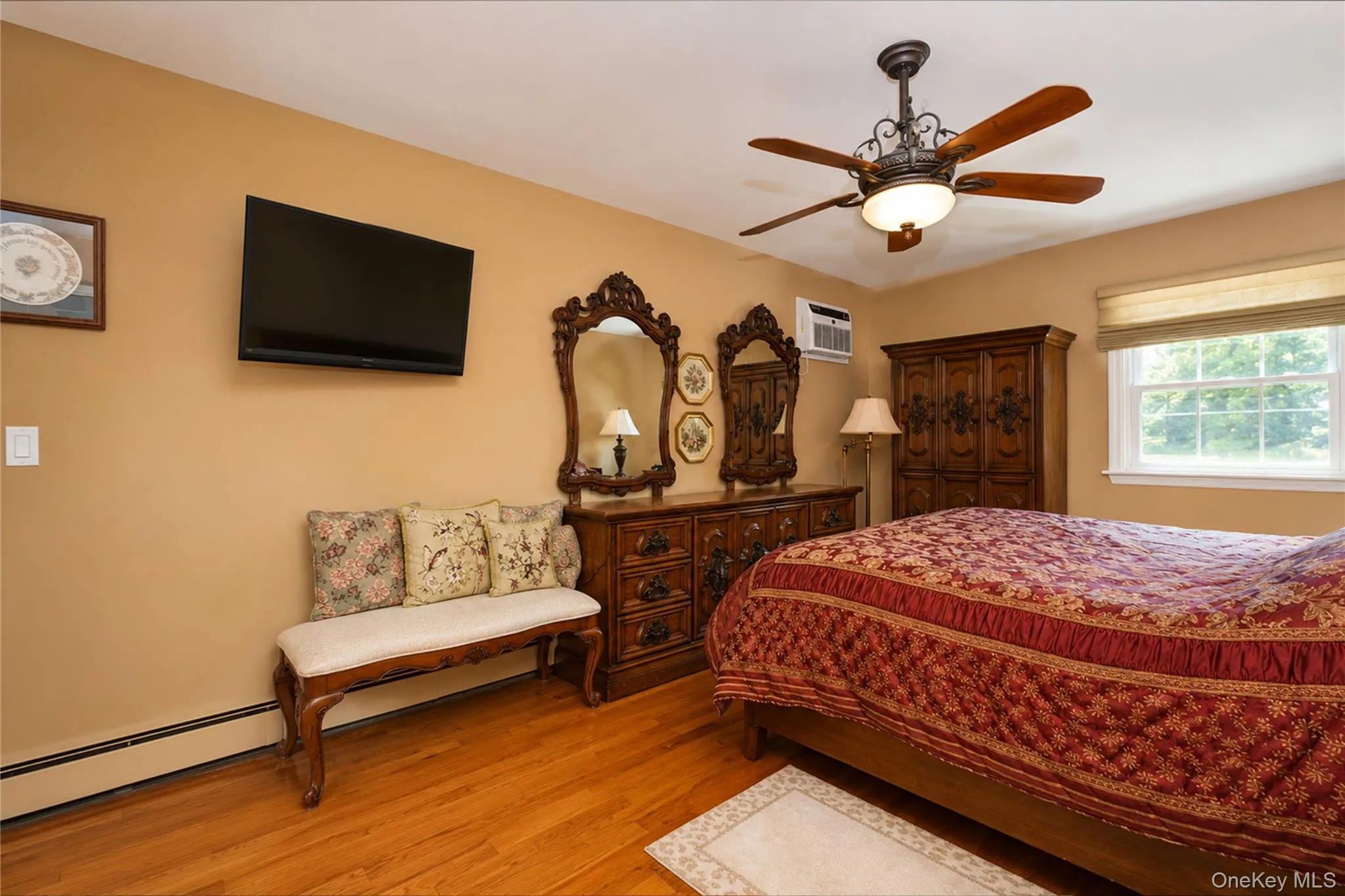 Hardwood flooring throughout featuring a ceiling fan with integrated lighting, a wall-mounted television, and baseboard heating Hardwood flooring throughout featuring a ceiling fan with integrated lighting, a wall-mounted television, and baseboard heating