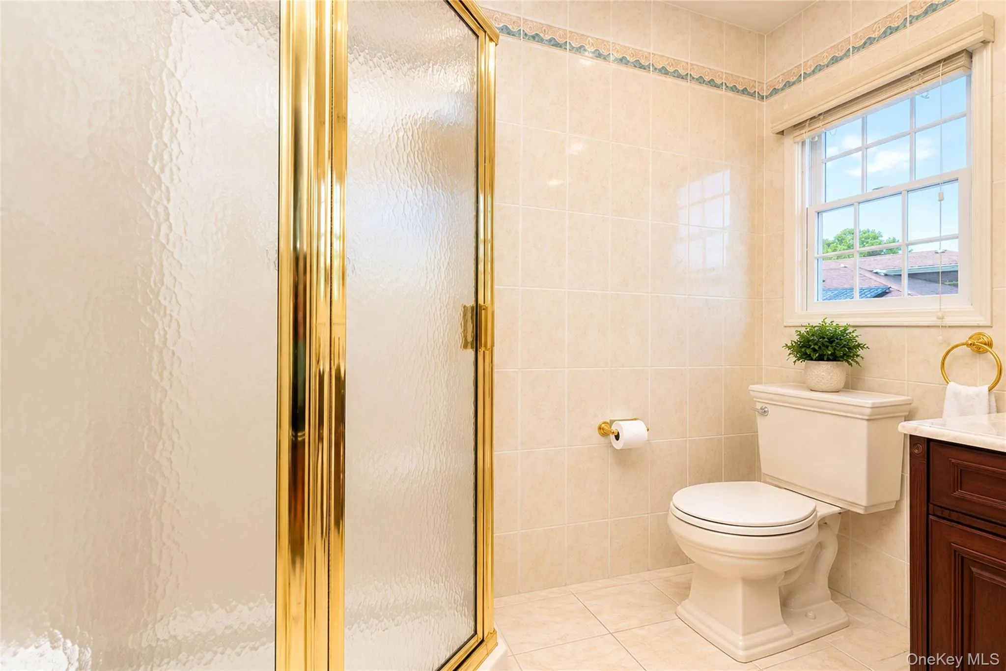 Shower enclosure with gold-tone framing and textured glass, complemented by ceramic tile flooring and wall-to-ceiling tiling Shower enclosure with gold-tone framing and textured glass, complemented by ceramic tile flooring and wall-to-ceiling tiling