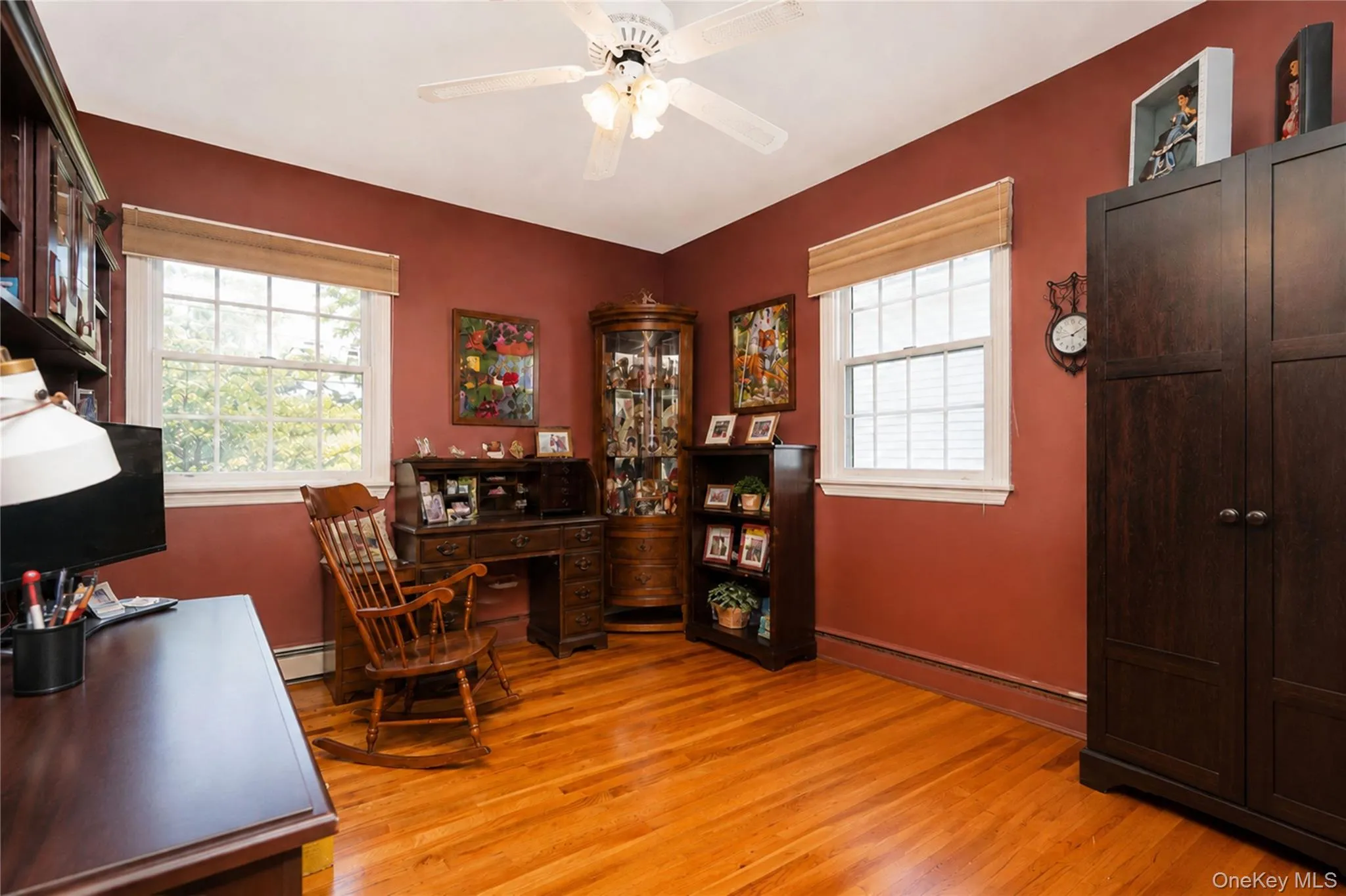 Bright room with wood-finish flooring, two large windows with blinds, a ceiling fan with integrated lighting, and rich red-toned walls Bright room with wood-finish flooring, two large windows with blinds, a ceiling fan with integrated lighting, and rich red-toned walls