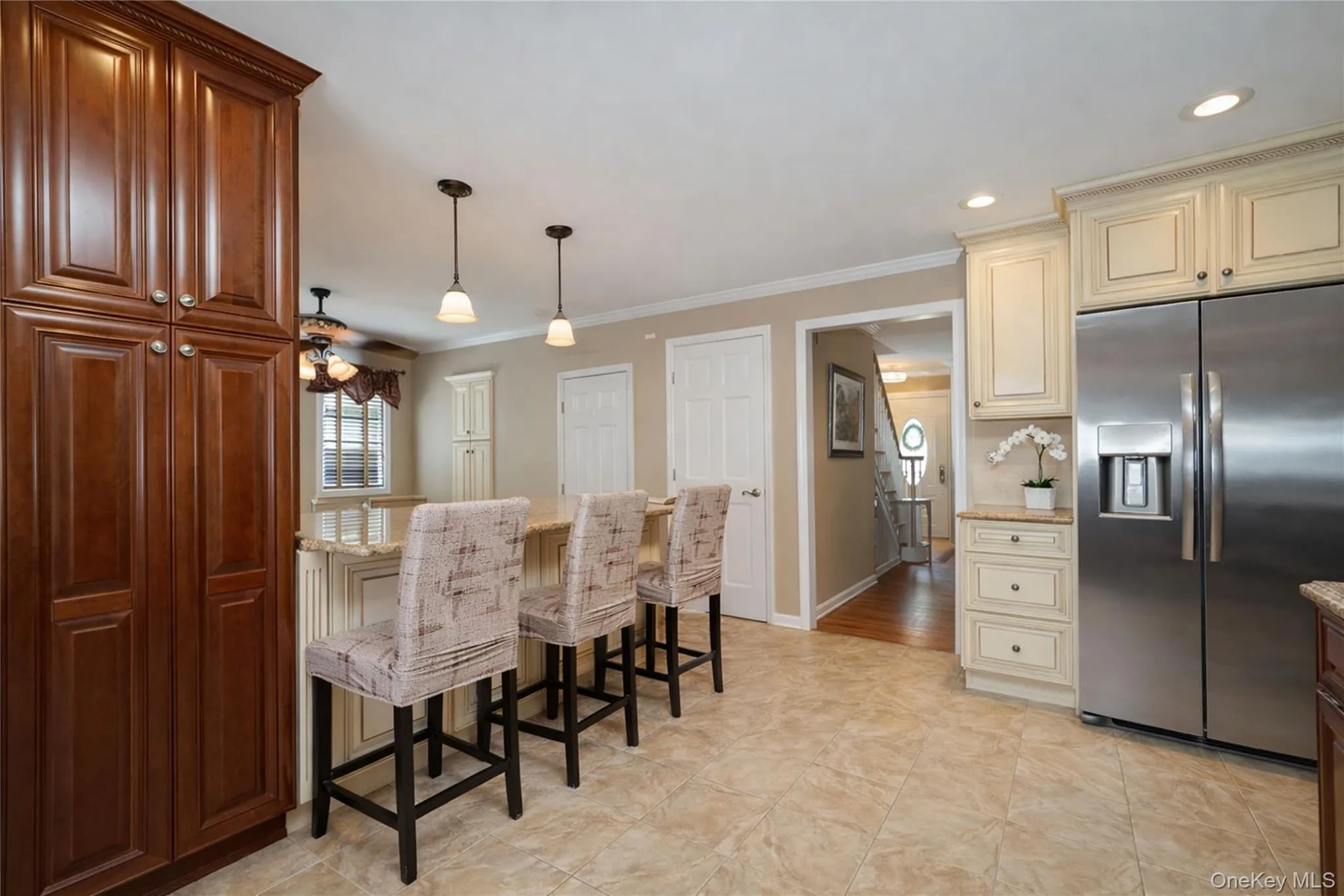 Kitchen featuring a large central island with pendant lighting, integrated stainless steel refrigerator, full-height dark wood cabinetry, and contrasting cream-colored upper and lower cabinetry Kitchen featuring a large central island with pendant lighting, integrated stainless steel refrigerator, full-height dark wood cabinetry, and contrasting cream-colored upper and lower cabinetry