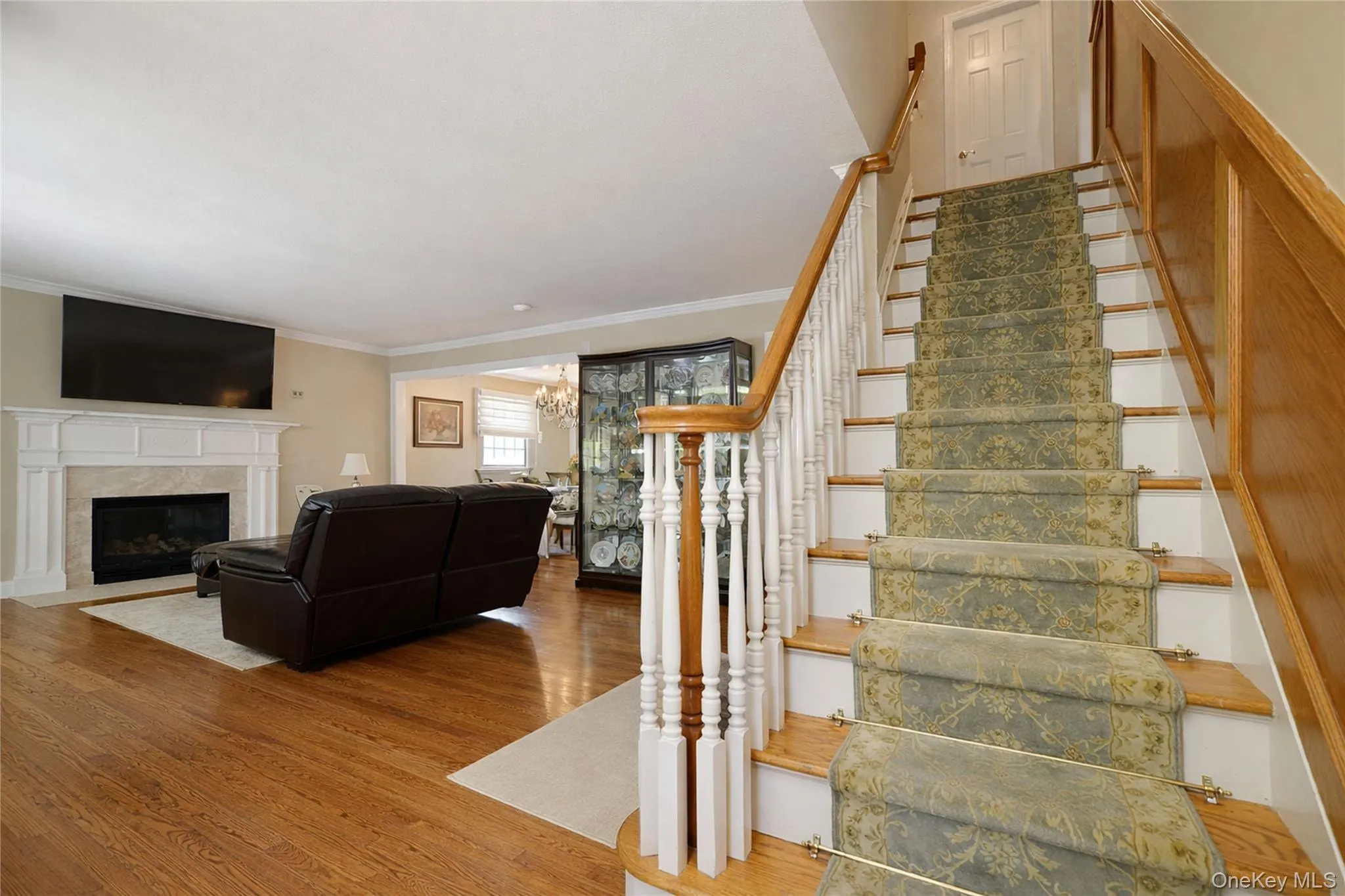 Hardwood flooring throughout the main living area, a decorative fireplace with a traditional mantel, and an open entryway staircase with a patterned runner Hardwood flooring throughout the main living area, a decorative fireplace with a traditional mantel, and an open entryway staircase with a patterned runner