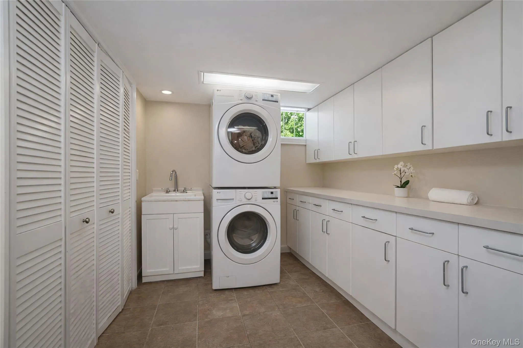 Dedicated utility room featuring extensive white cabinetry, a utility sink, and stacked laundry appliances Dedicated utility room featuring extensive white cabinetry, a utility sink, and stacked laundry appliances